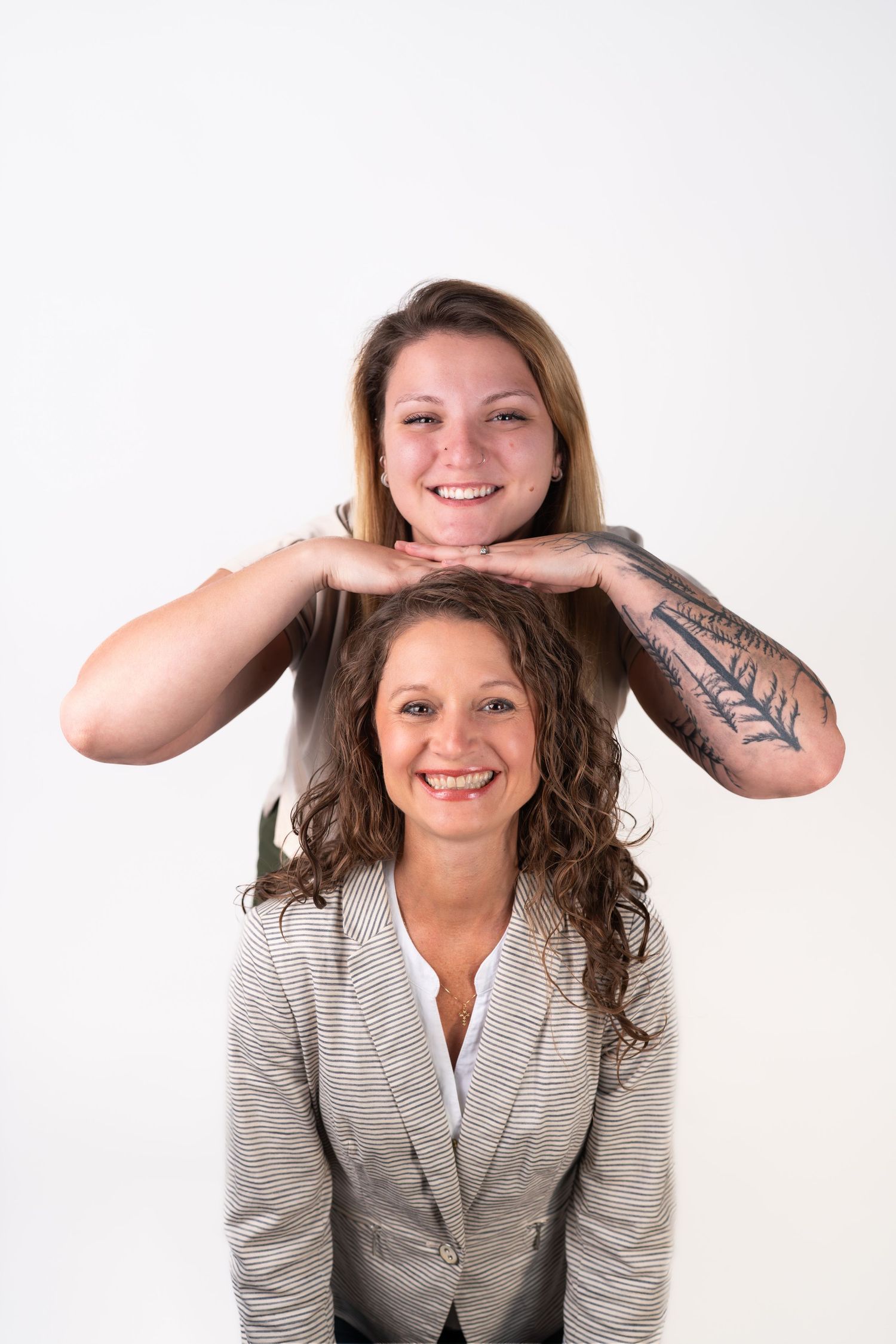 Two people in business attire pose playfully against white studio background.