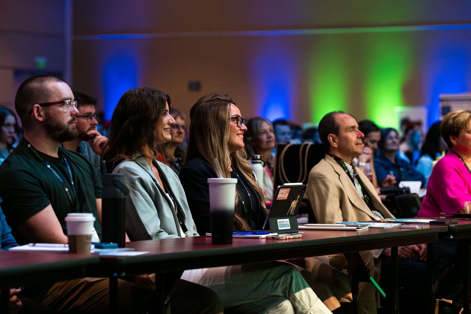 Conference audience seated in rows with colorful ambient lighting.