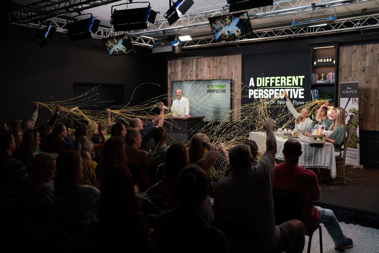 Dark auditorium with crowd facing illuminated stage displaying 'A Different Perspective' sign.