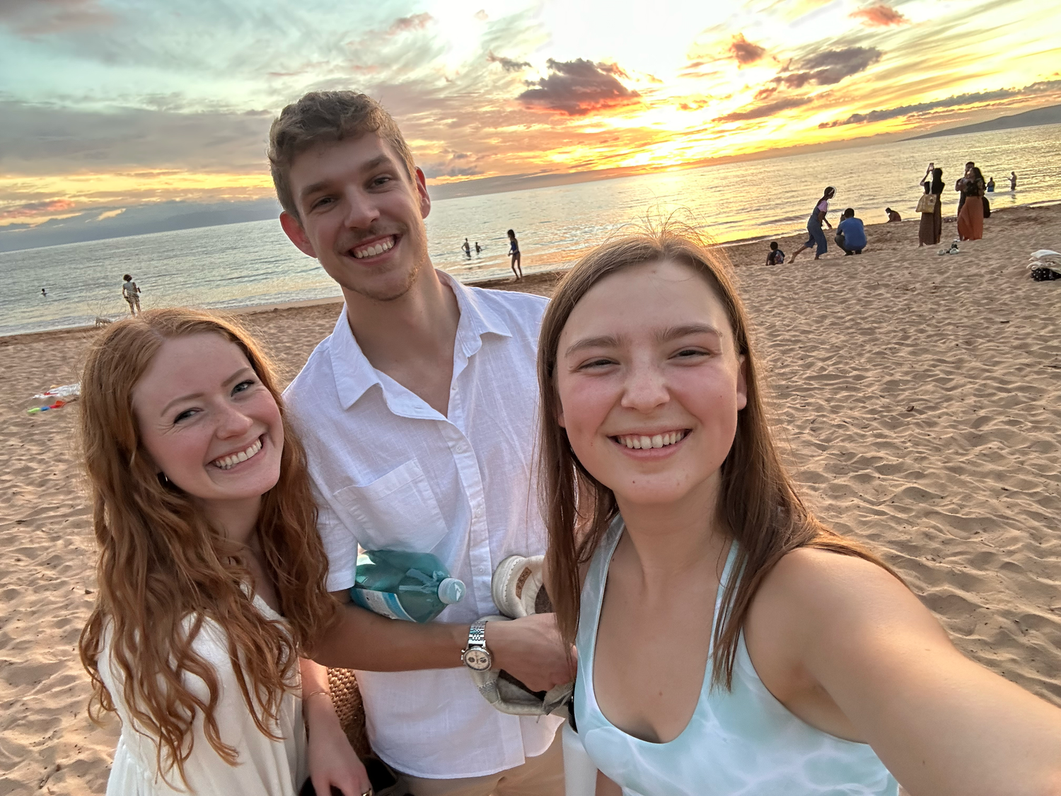 Group enjoying sunset together on a sandy beach with golden sky in background.