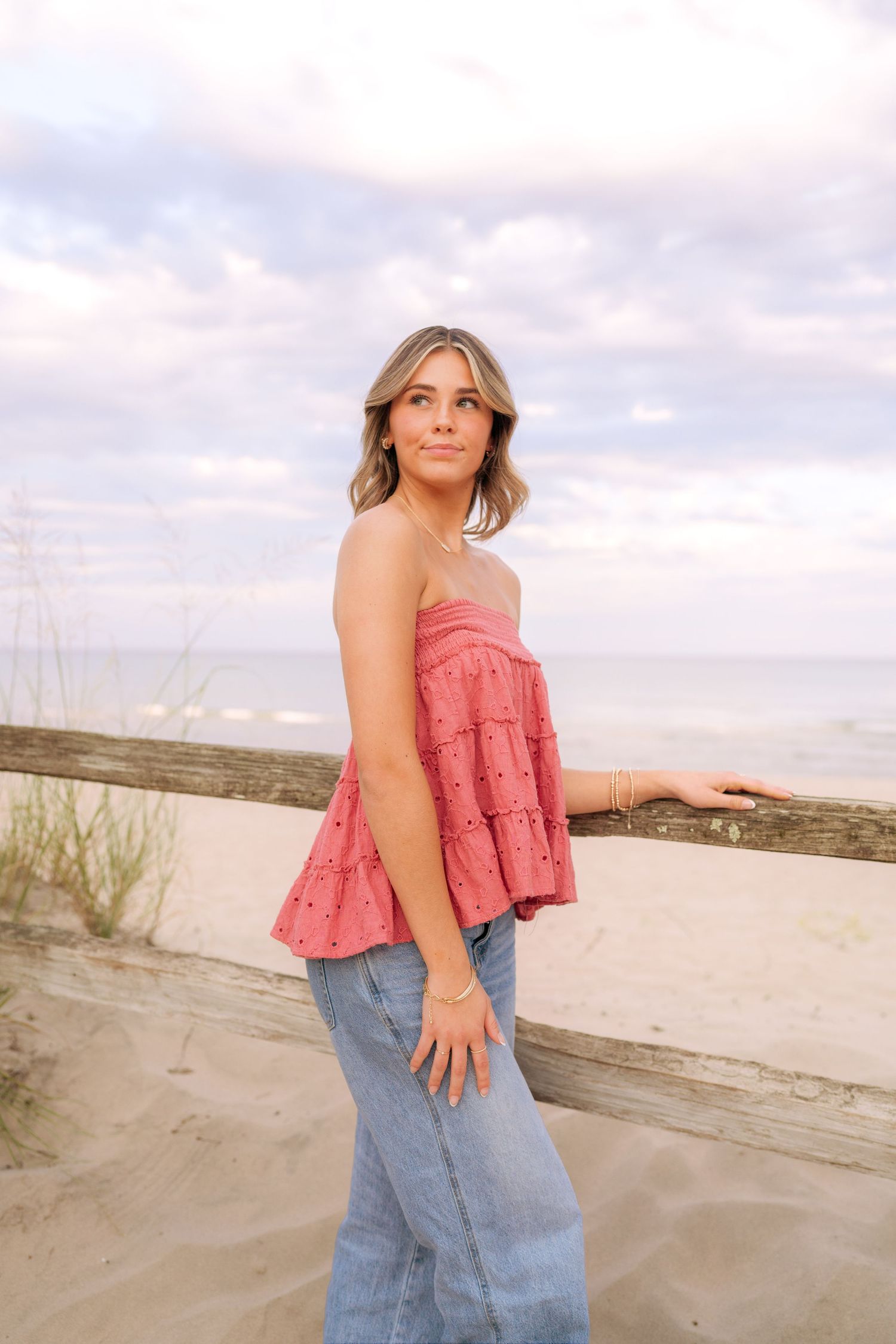 Woman in pink ruffle top and jeans posing against concrete wall at beach.