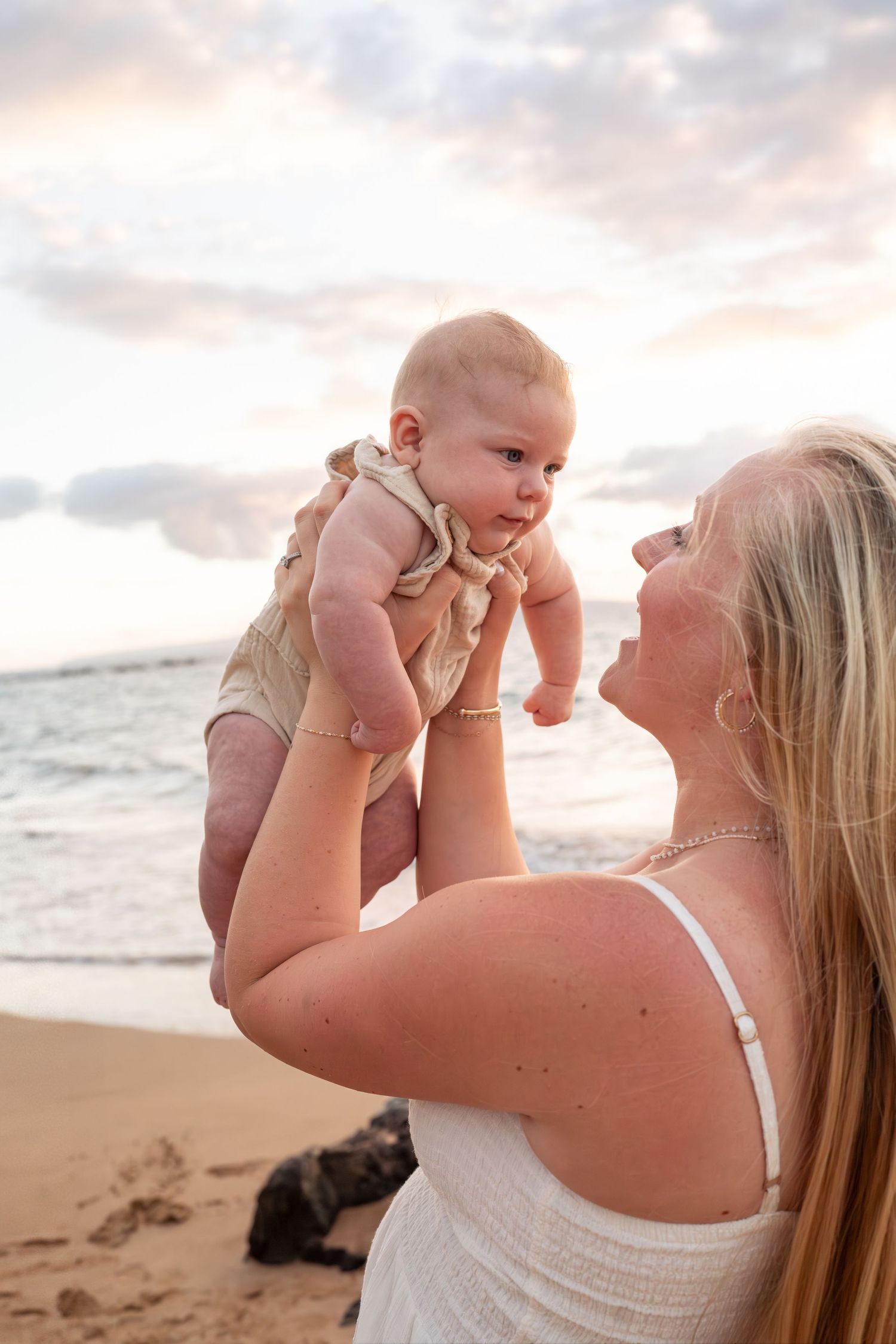 Mother and baby sharing joyful moment together on beach at sunset.