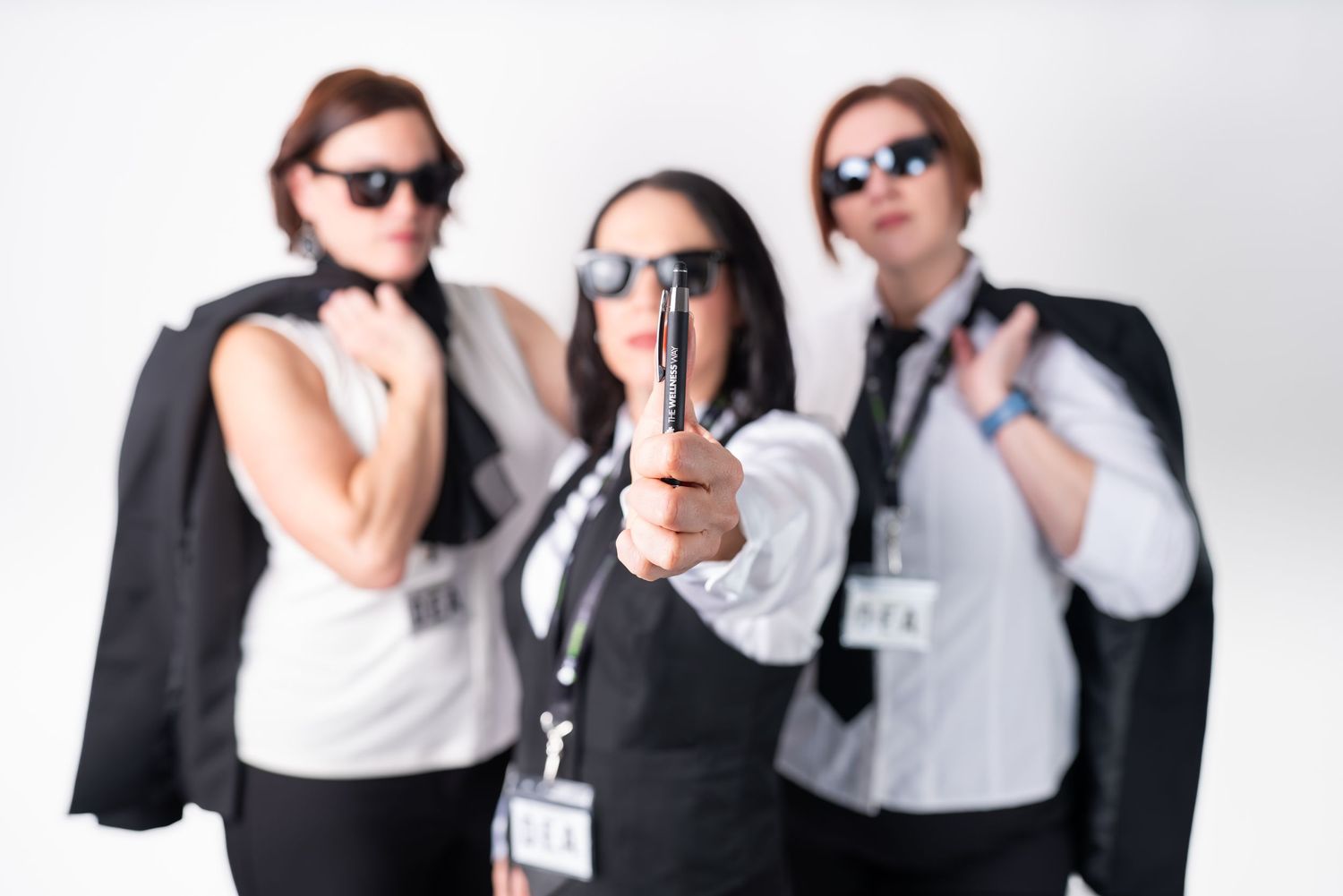 Three people in business attire and sunglasses pose confidently against a white background.