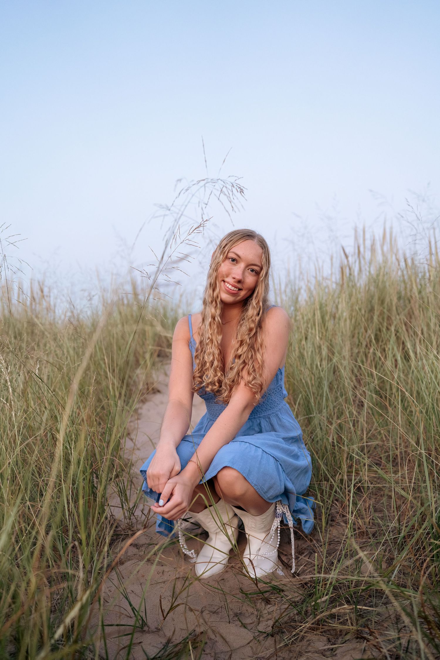Figure in blue dress crouches among tall beach grass on a sunny day.
