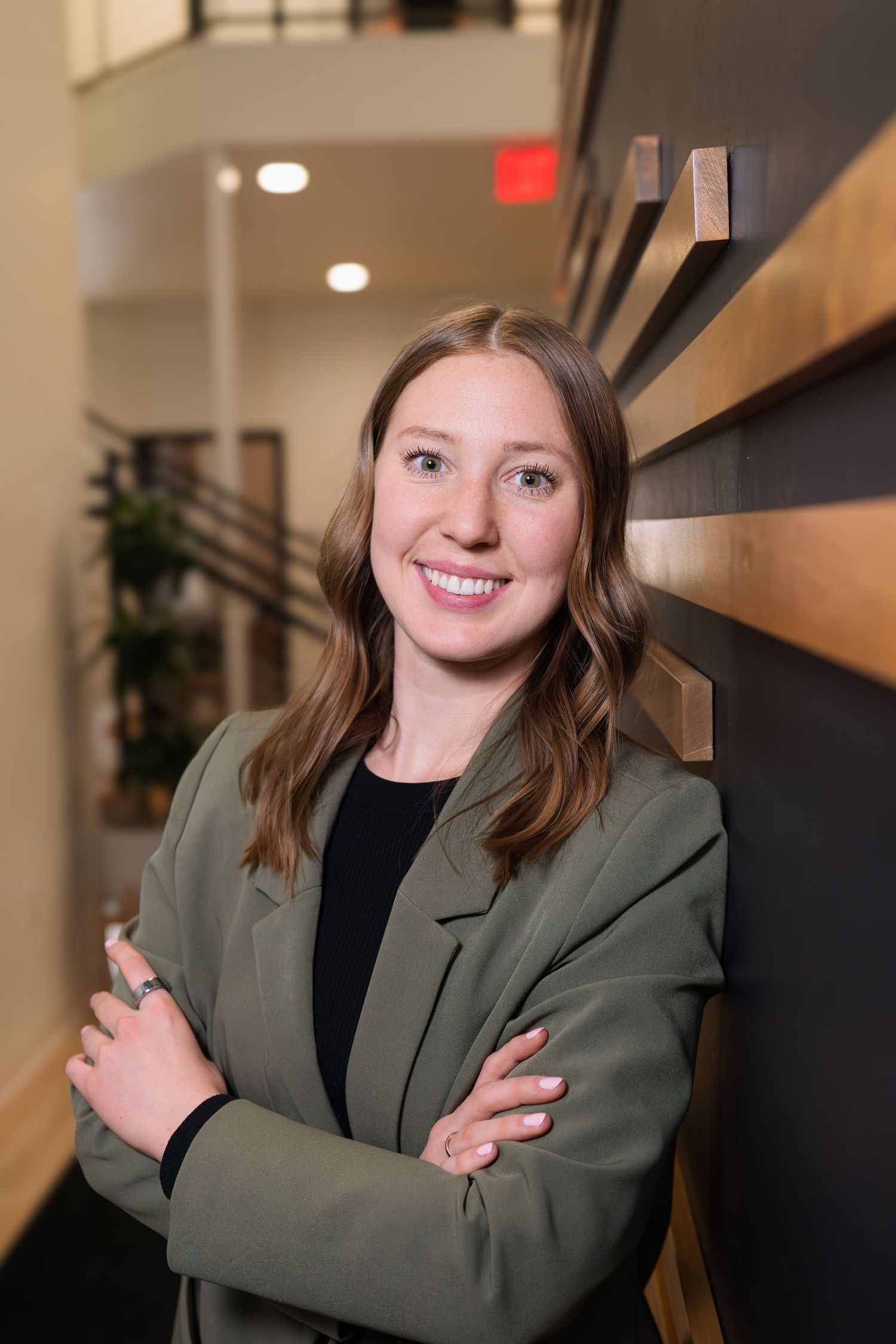 Professional headshots in an office hallway wearing a green blazer and black top.