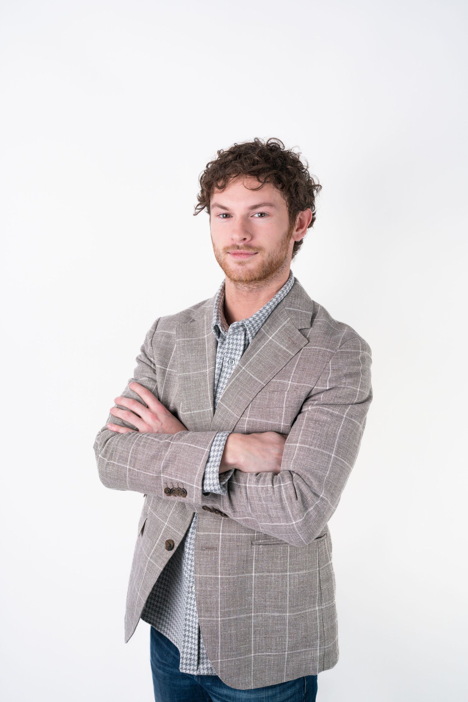 Model wearing grey plaid blazer and checkered shirt poses confidently against white backdrop.