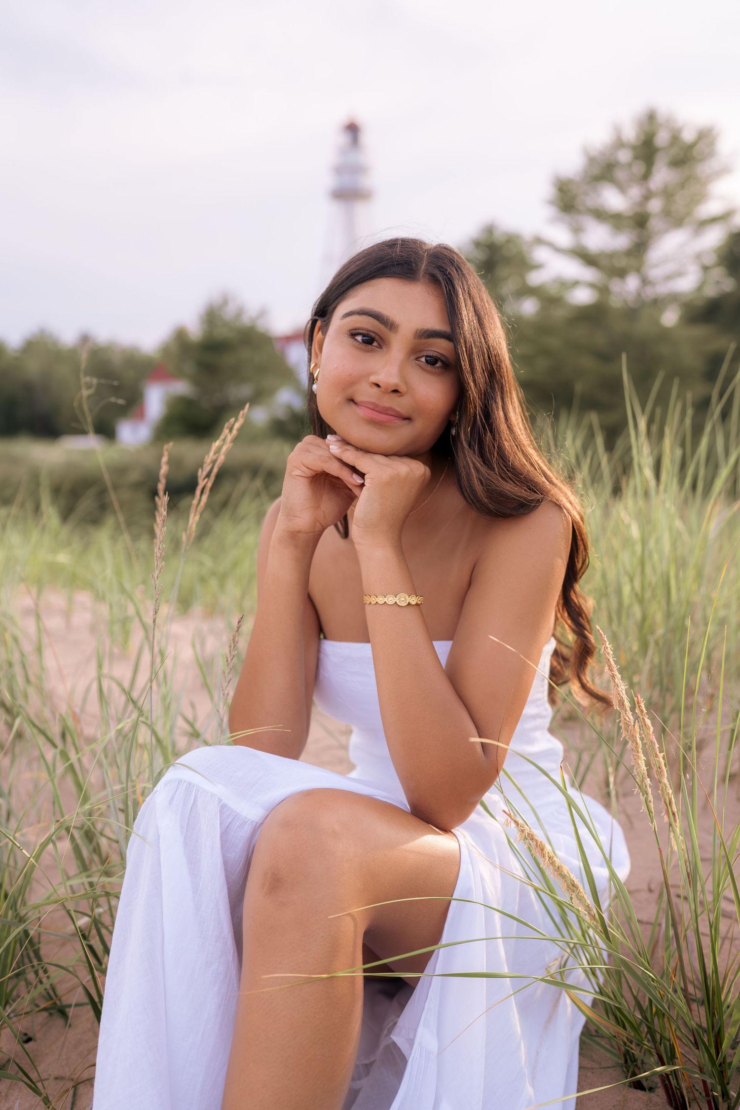 Person in white dress sitting among coastal grass during golden hour.