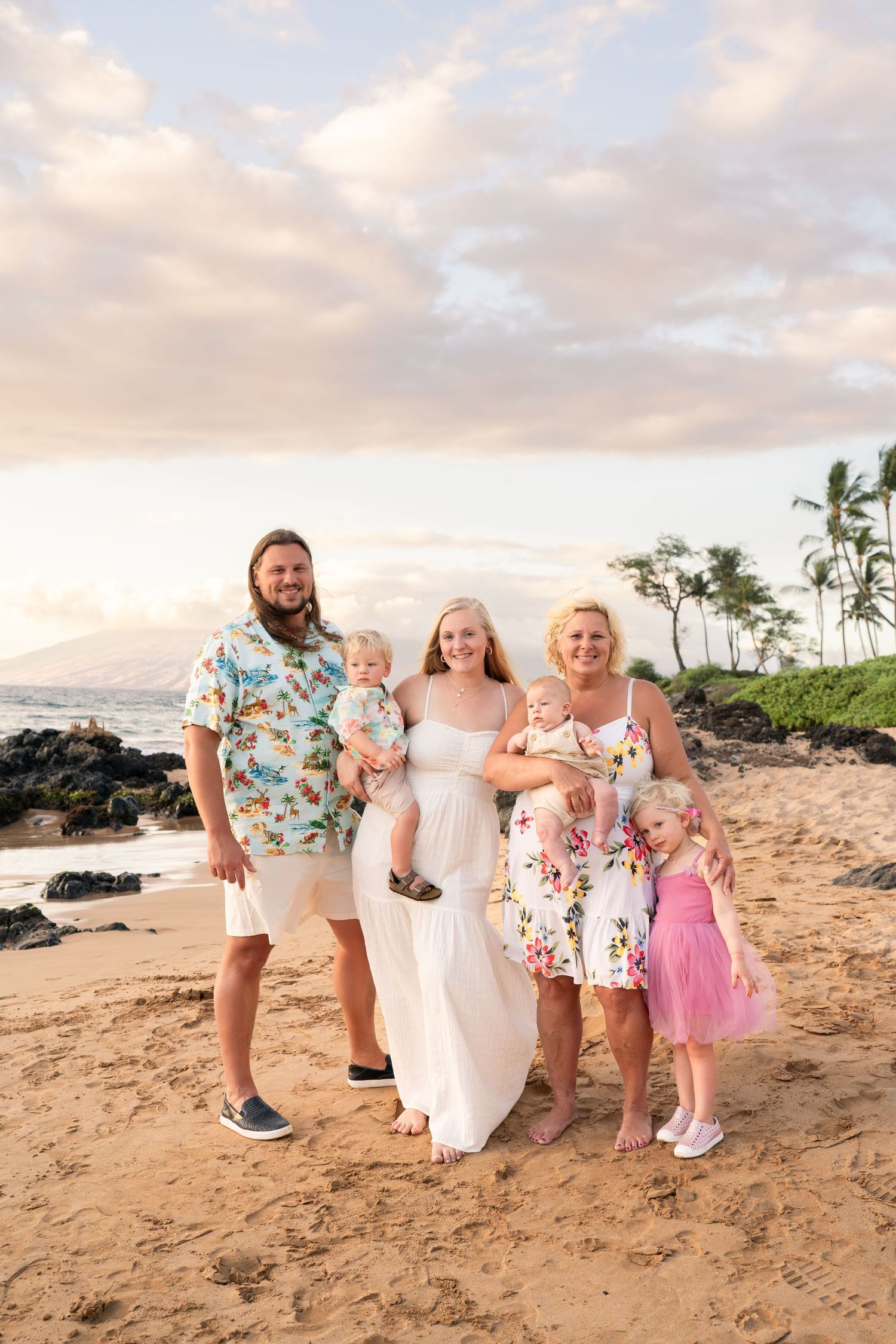 Family group photo on sandy beach with ocean and palm trees in background.