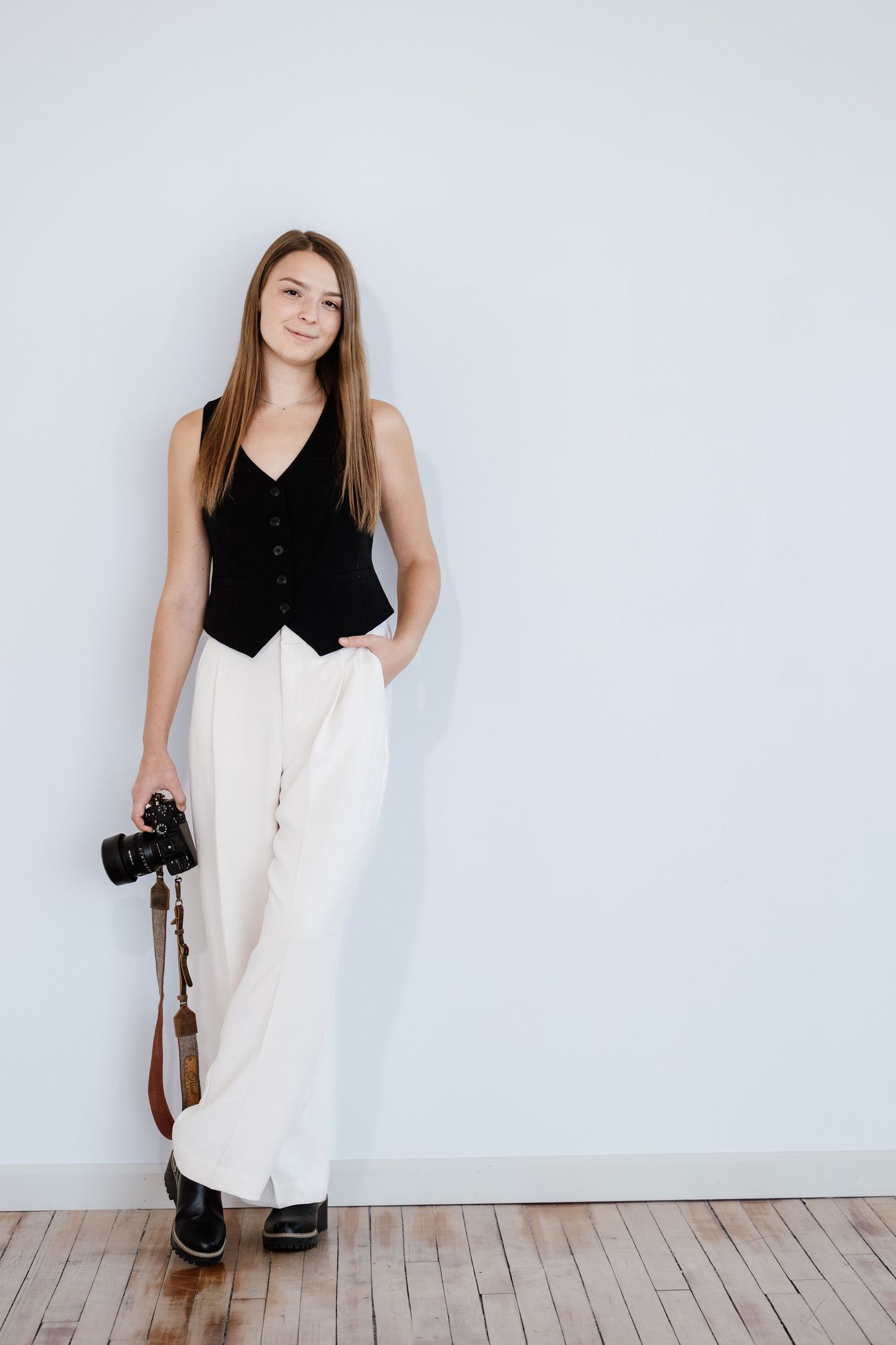 Creative portrait session showing photographer with camera against white wall and wooden floor.