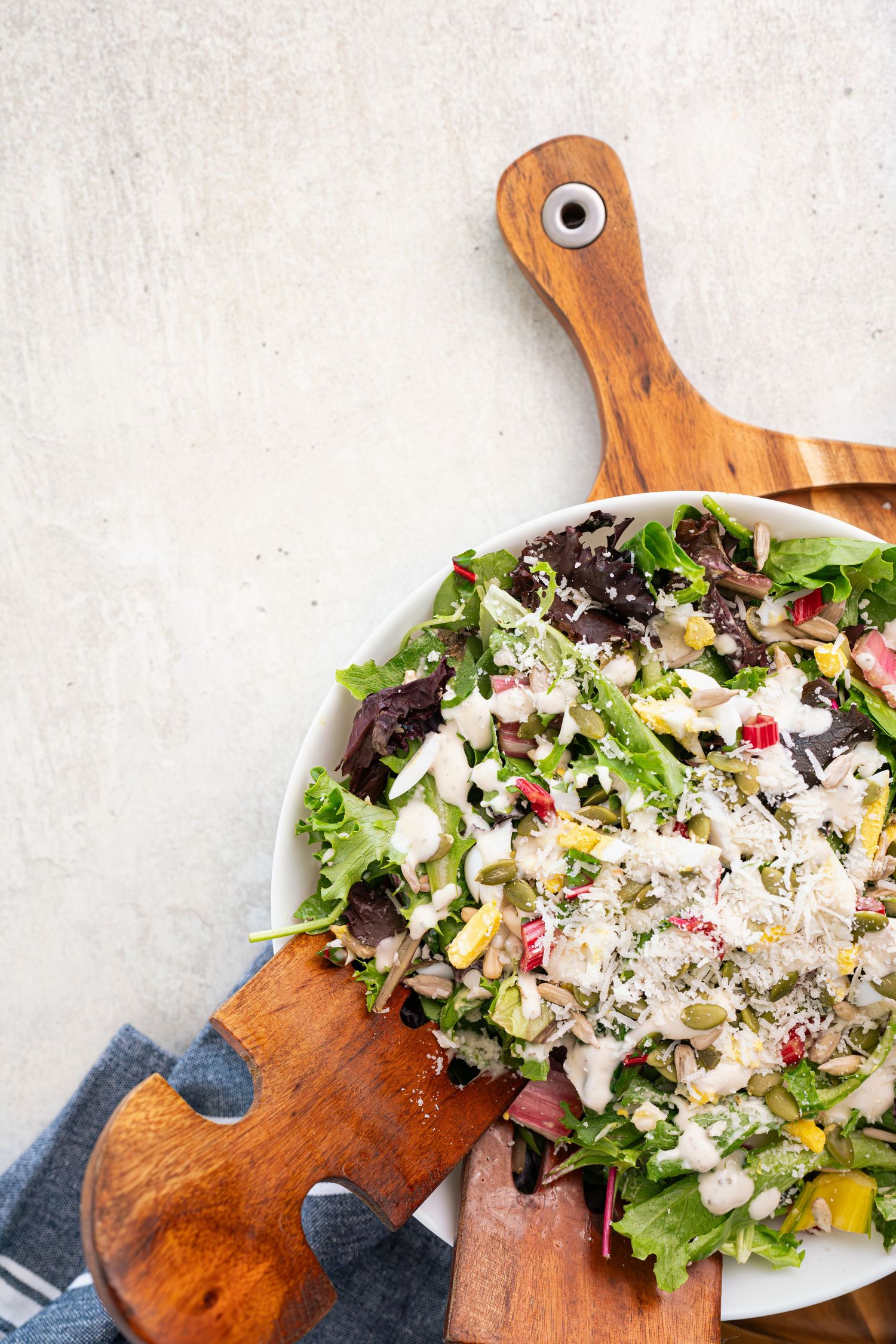 Fresh garden salad with shaved parmesan cheese served on wooden puzzle-shaped cutting board.