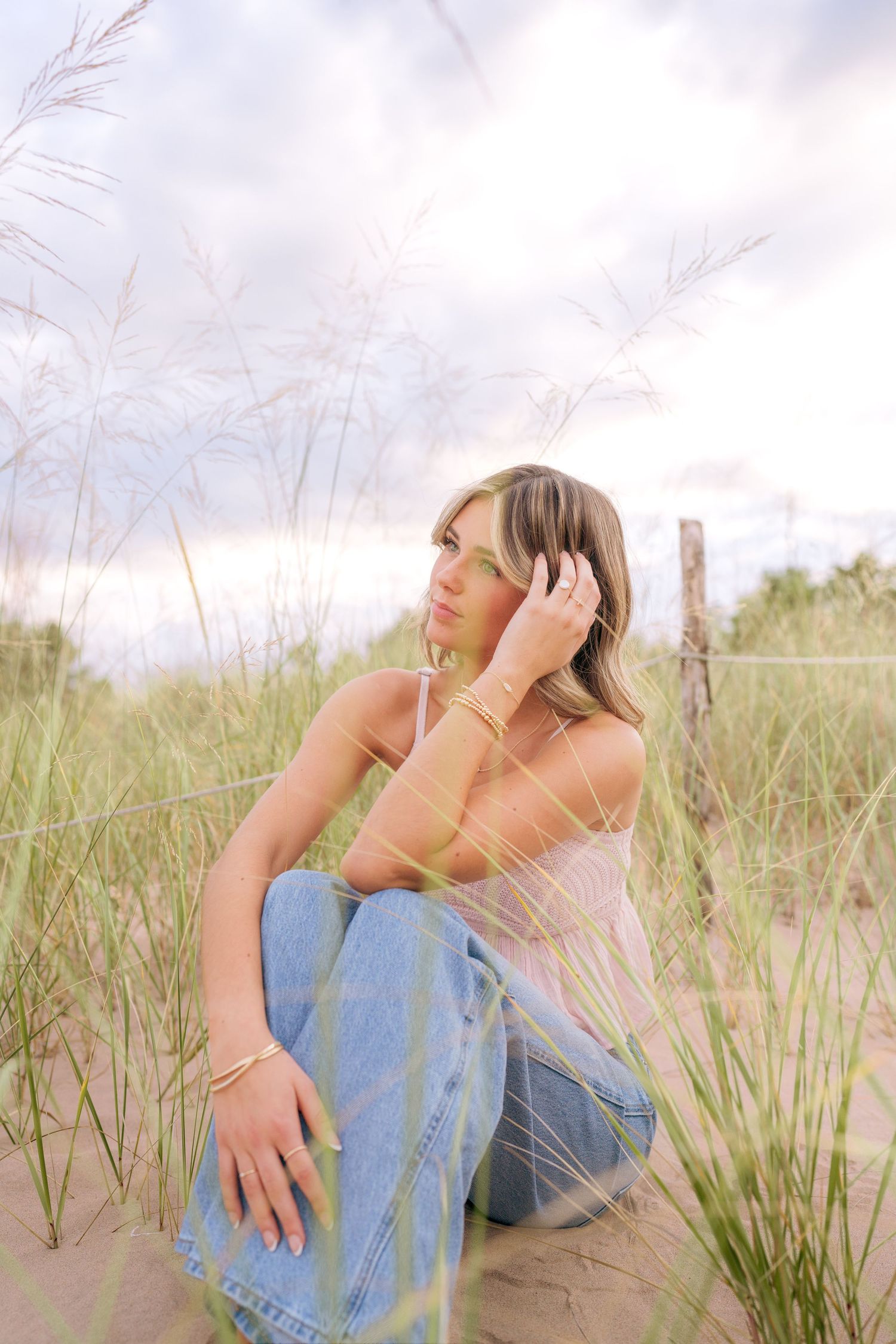 Artistic portrait series in beach grass showing soft contemplative poses in casual denim and warm lighting.