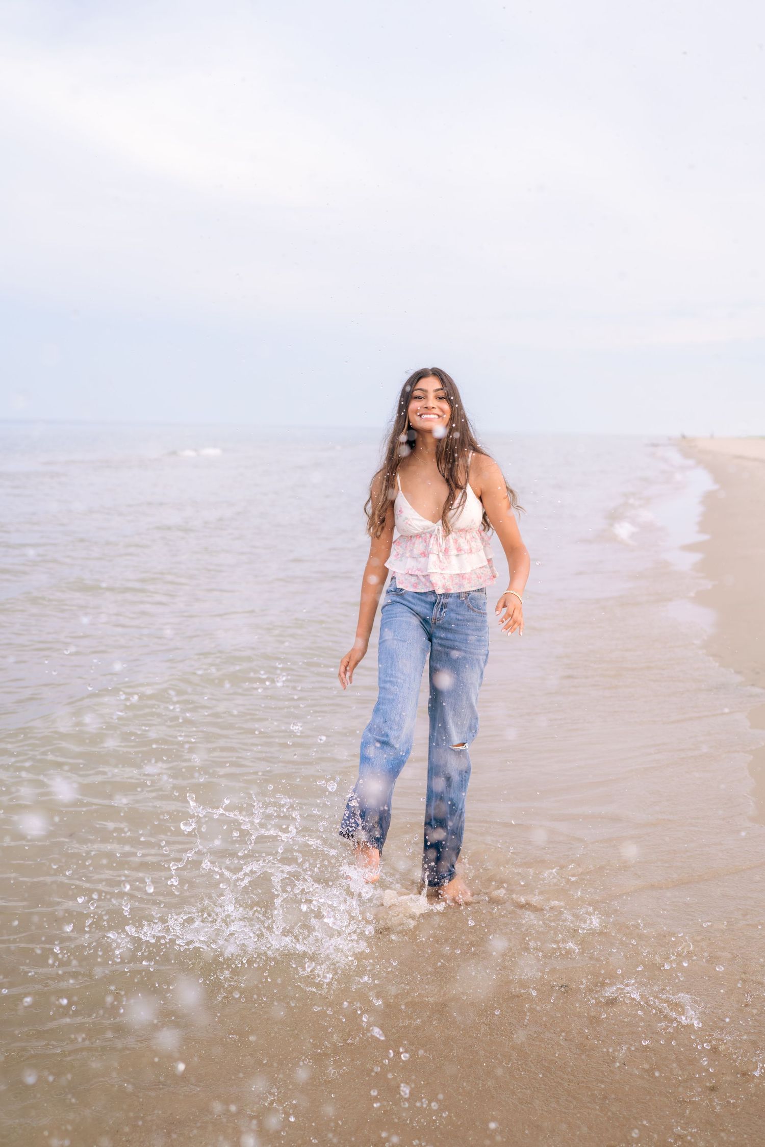 Someone splashes in shallow beach water wearing jeans and a white top.