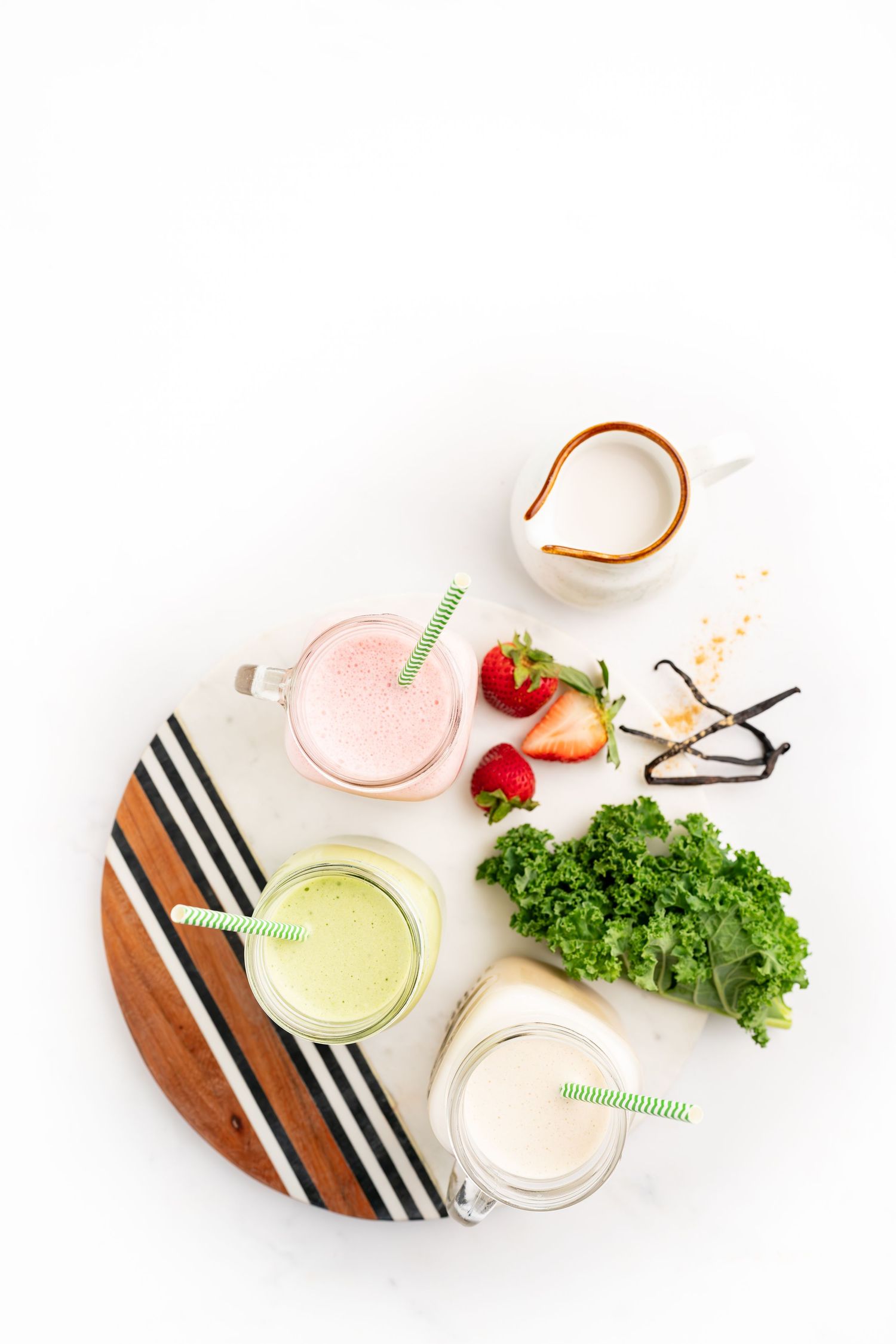 Healthy smoothies in mason jars on striped cutting board with fresh strawberries and greens.