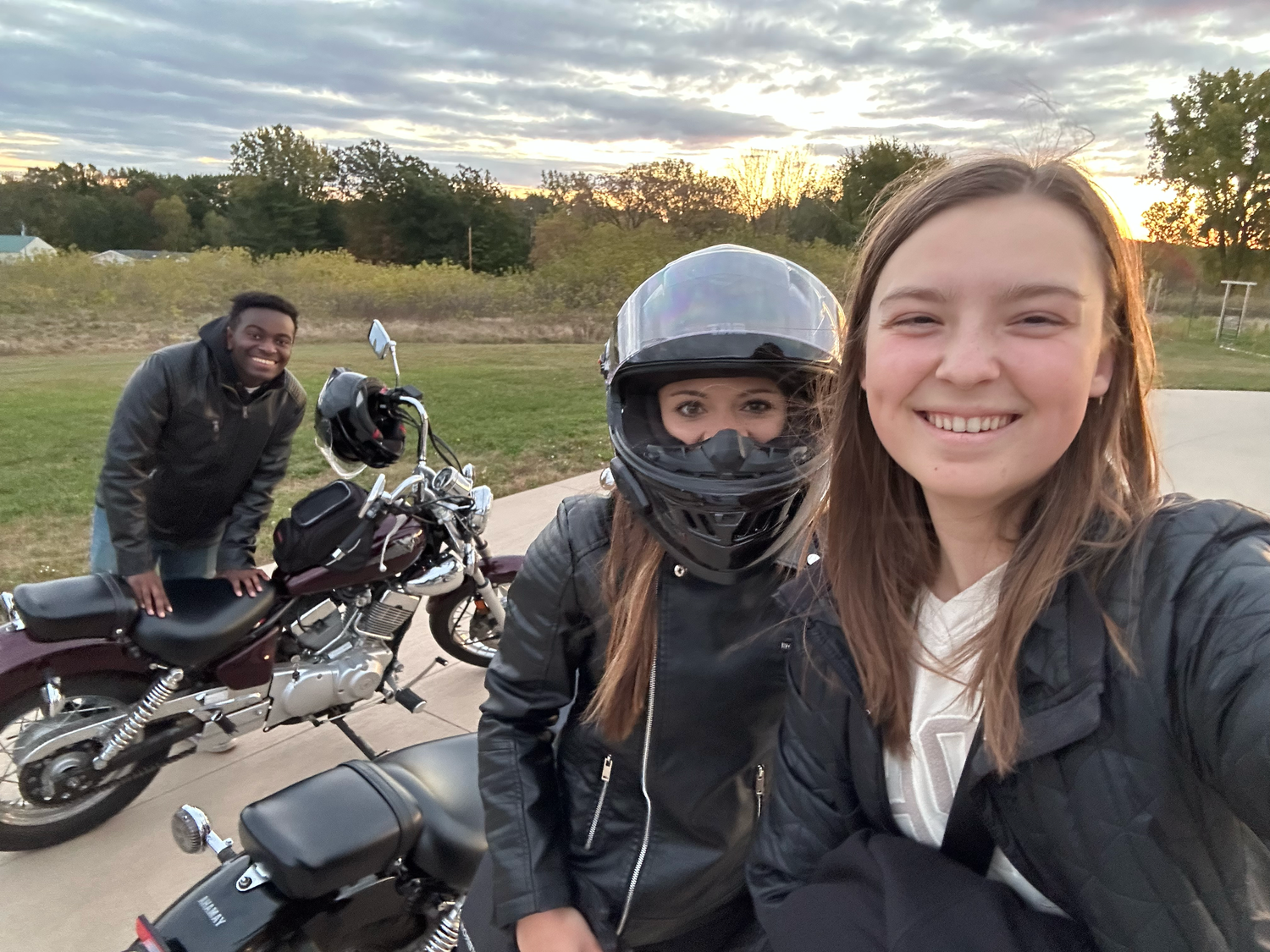 A group poses near motorcycles at sunset for an outdoor photo.