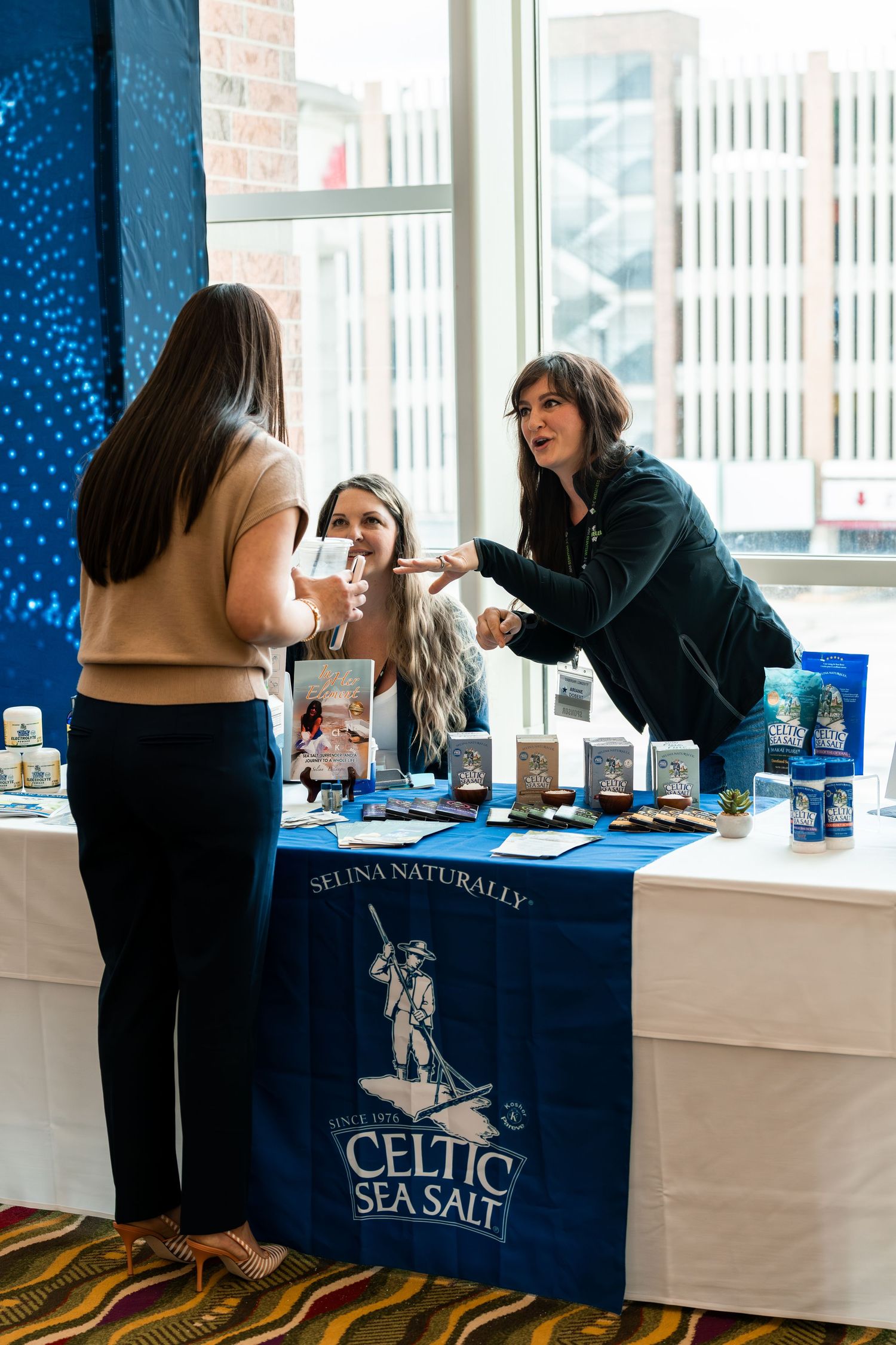 Vendor booth displaying Celtic Sea Salt products with customers at a trade show.