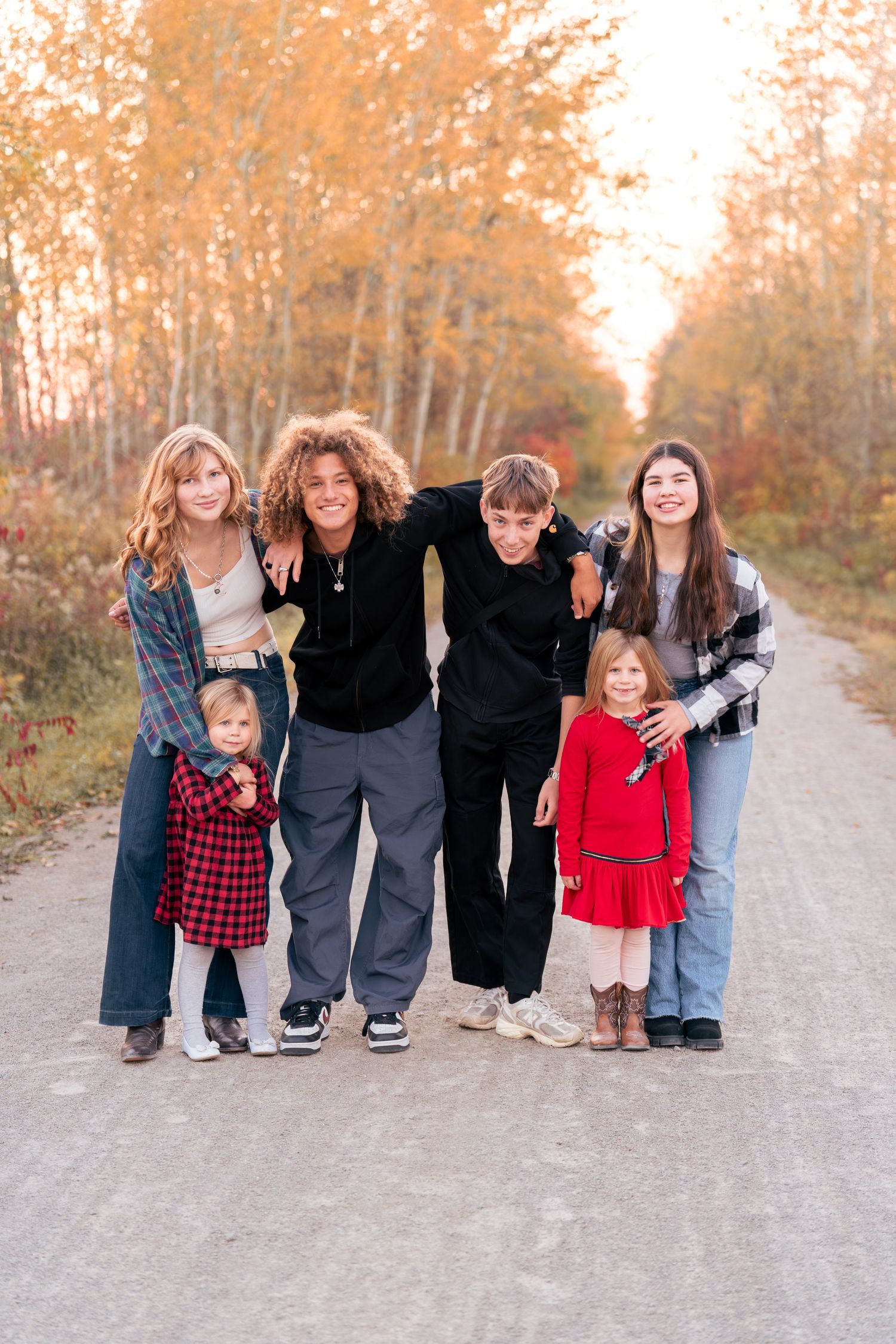Casual family portrait on sandy path with fall foliage in background.