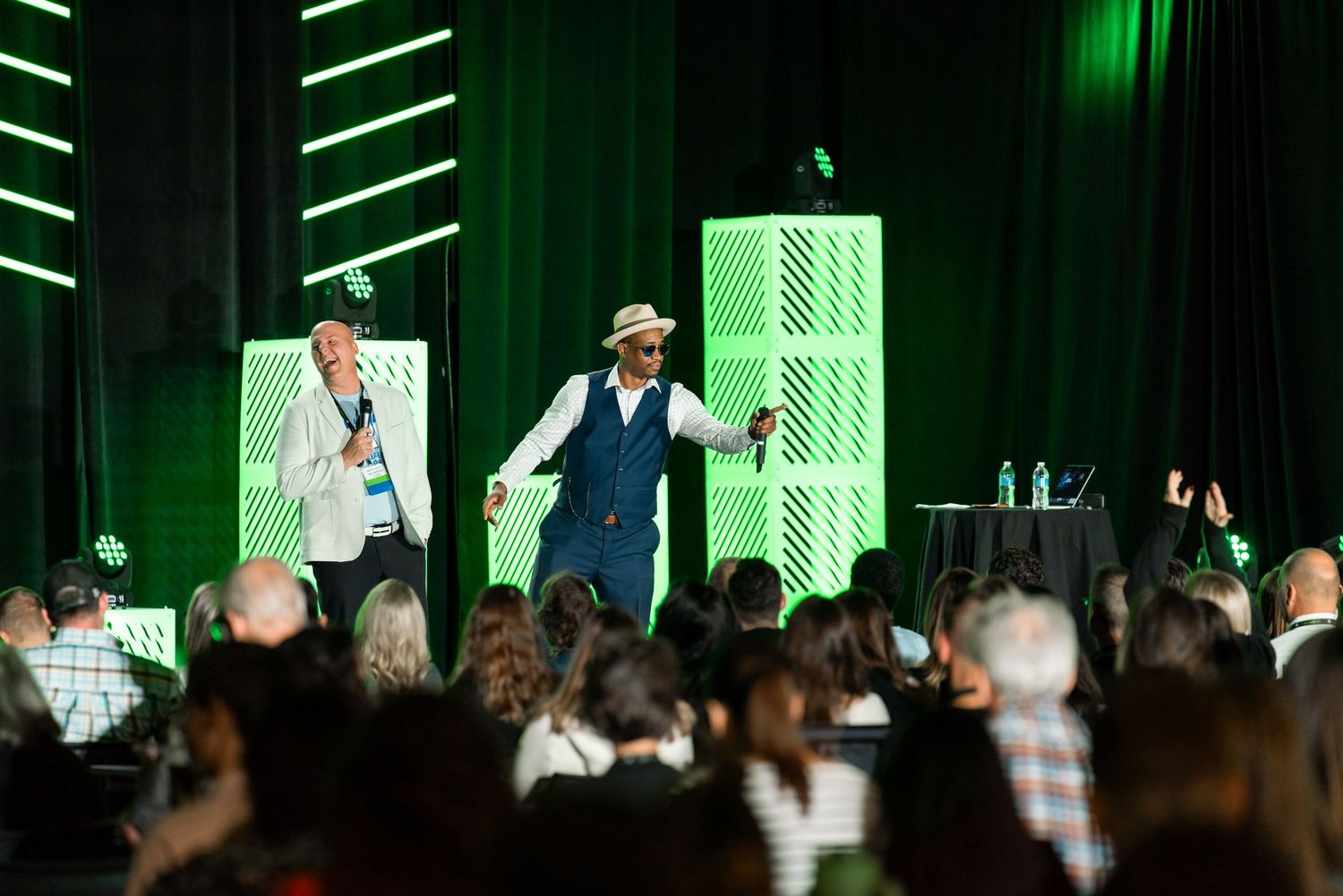 Wide shot of a conference stage with green lighting and white geometric panels in the background.