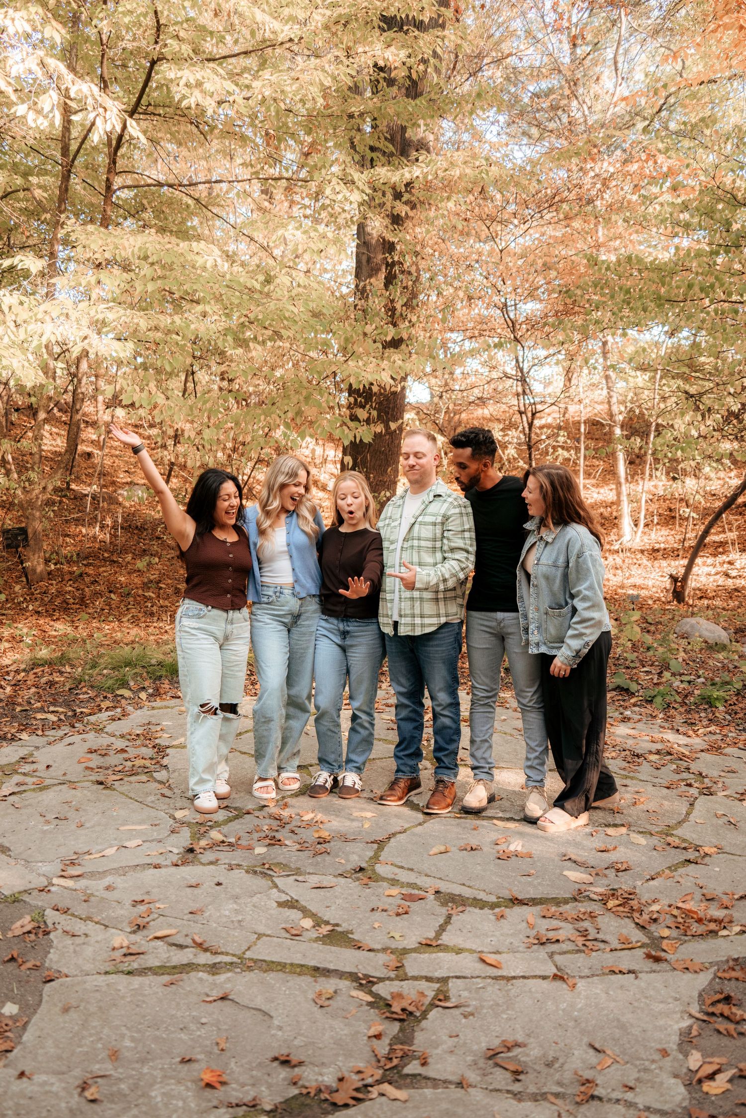 Friends in casual denim and sweaters stand together on a rocky path during autumn.