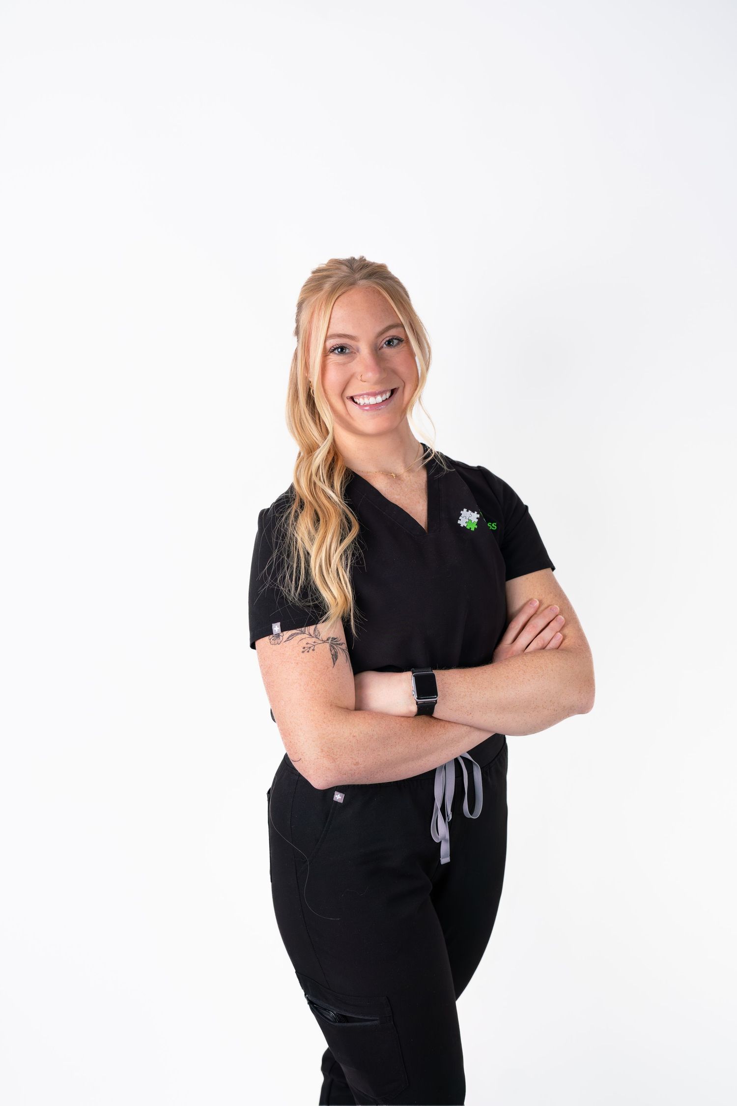 Healthcare worker in black scrubs poses with crossed arms against white background.