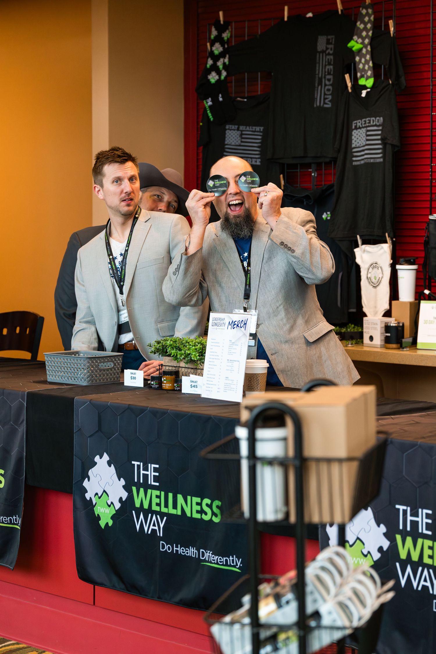 Conference vendors at booth with Wellness Way branded display table.