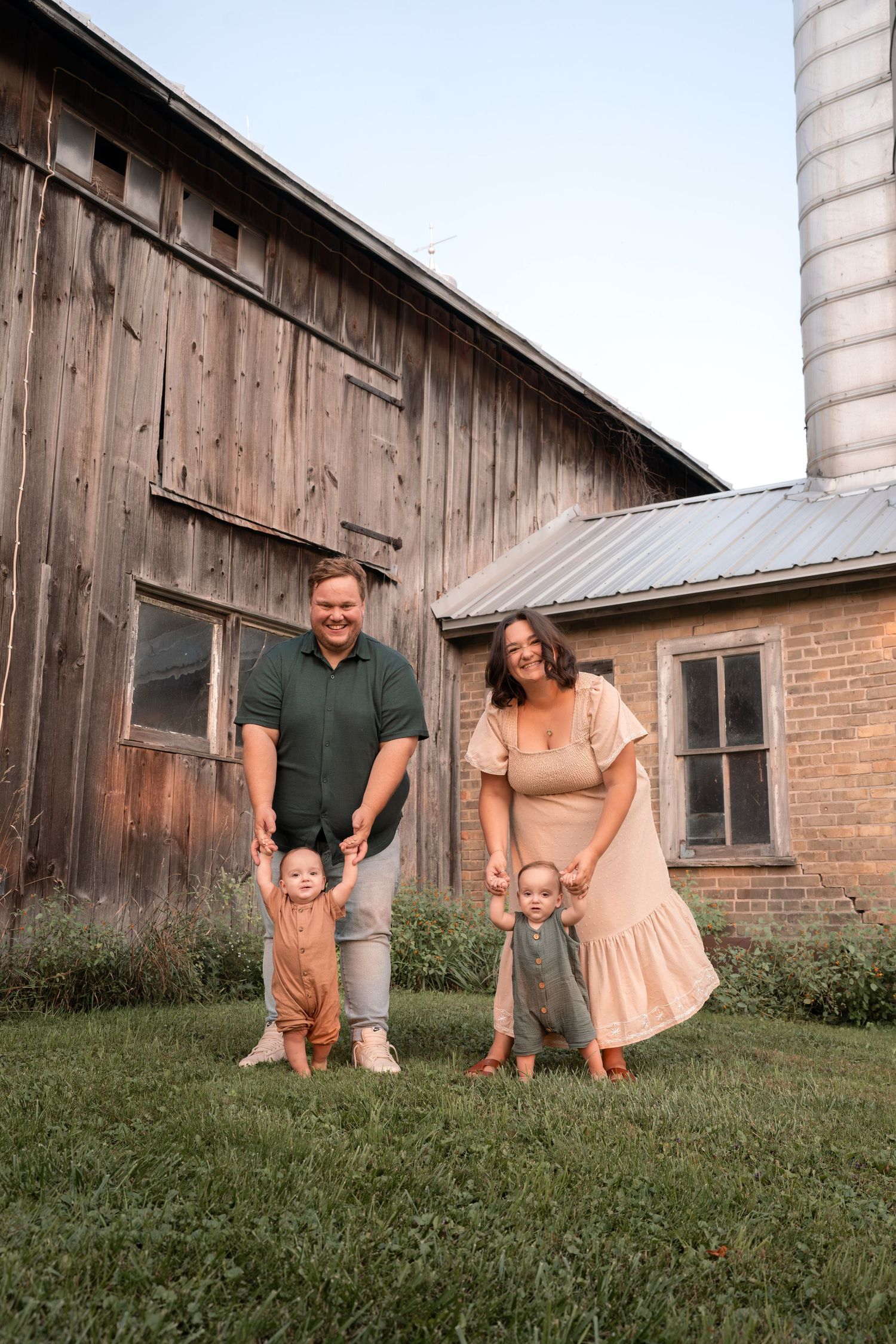 Family playing and laughing together on grassy hill near rustic barn.