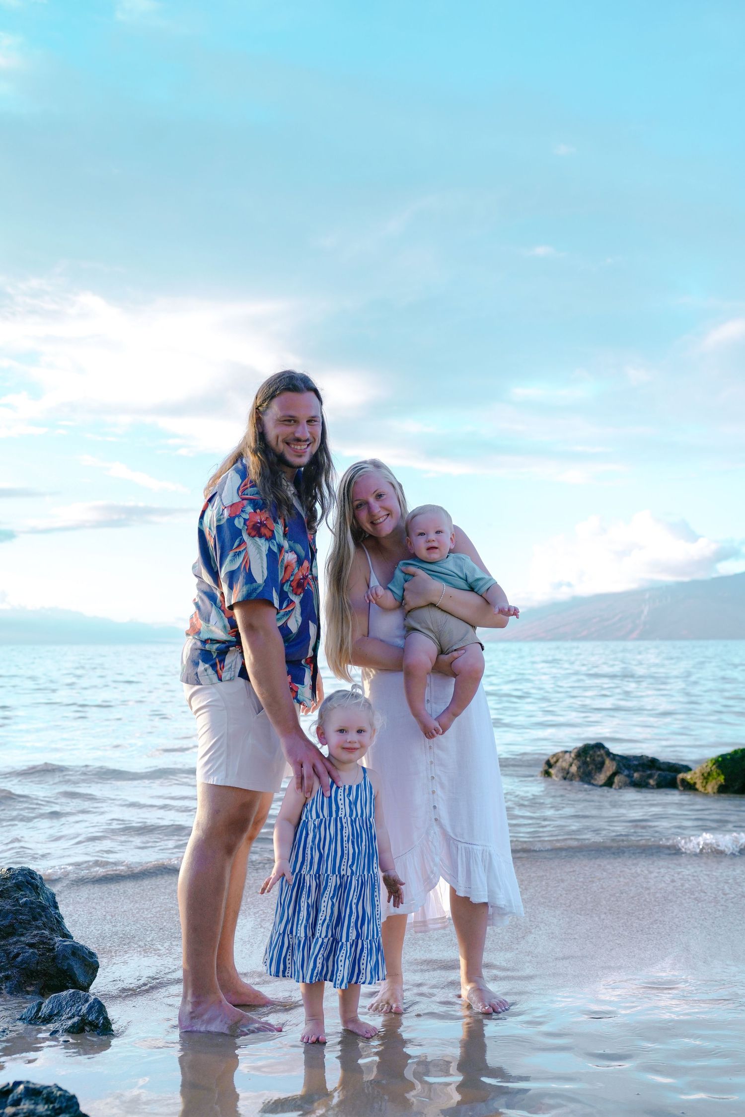Family playing together in shallow ocean water at sunset.