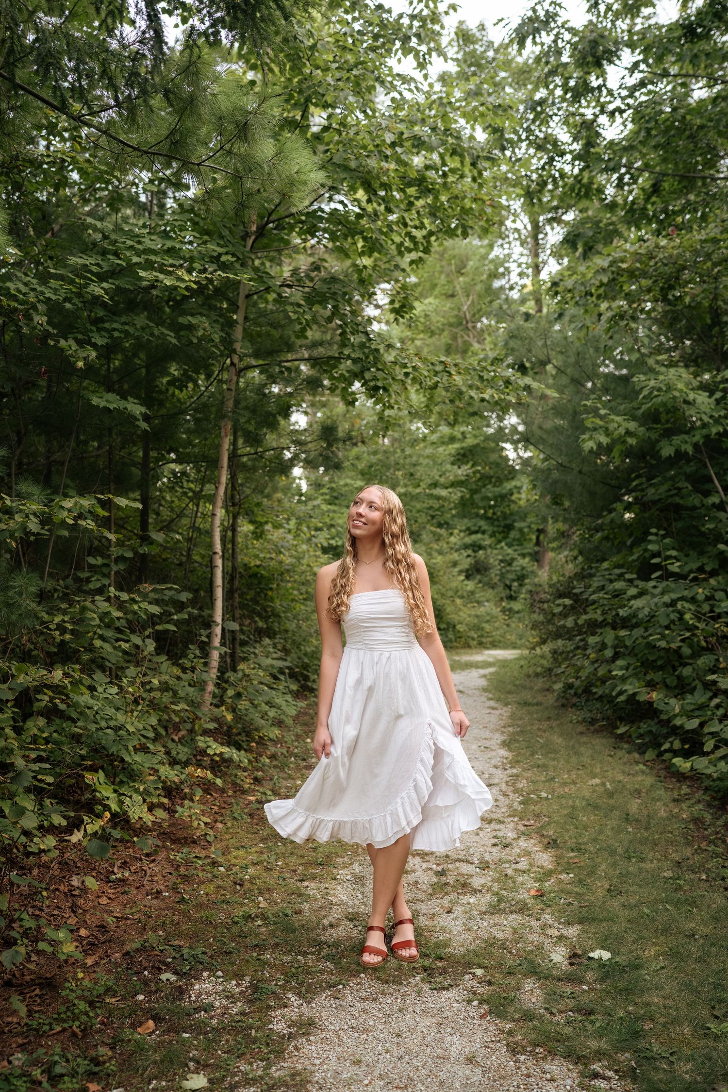 White dress flowing as someone walks down a tree-lined gravel path.