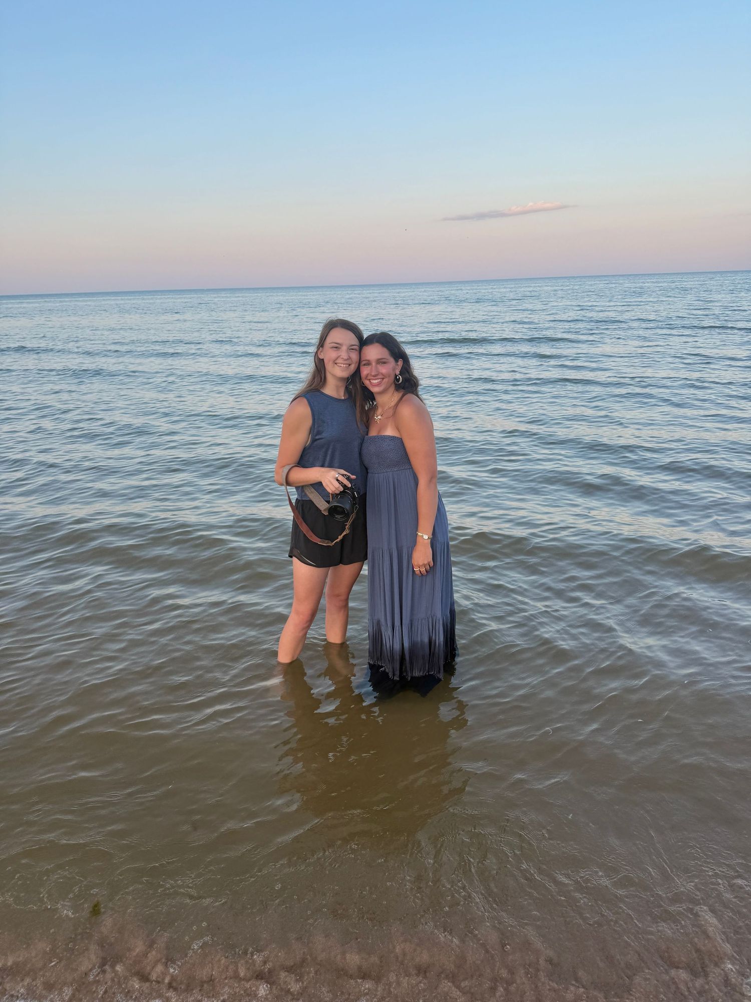 People wading in calm waters at the beach during sunset.