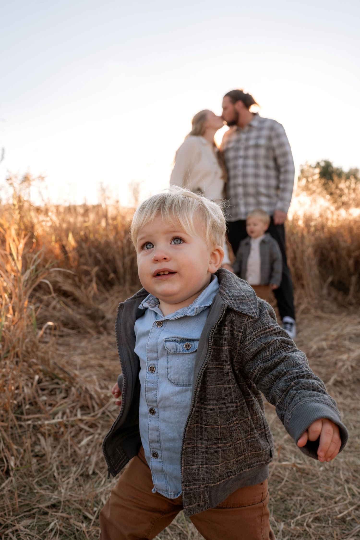 Toddler in plaid jacket and denim shirt smiles in autumn field.