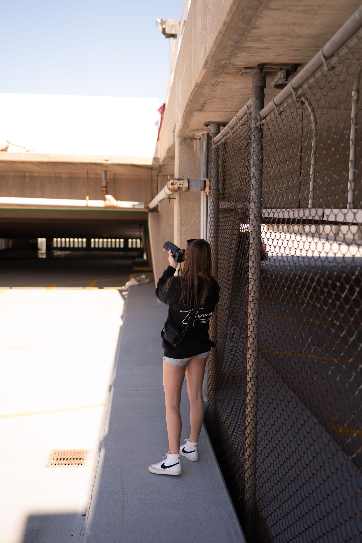 Person taking photos in a long hallway with chain link fence and white walls.