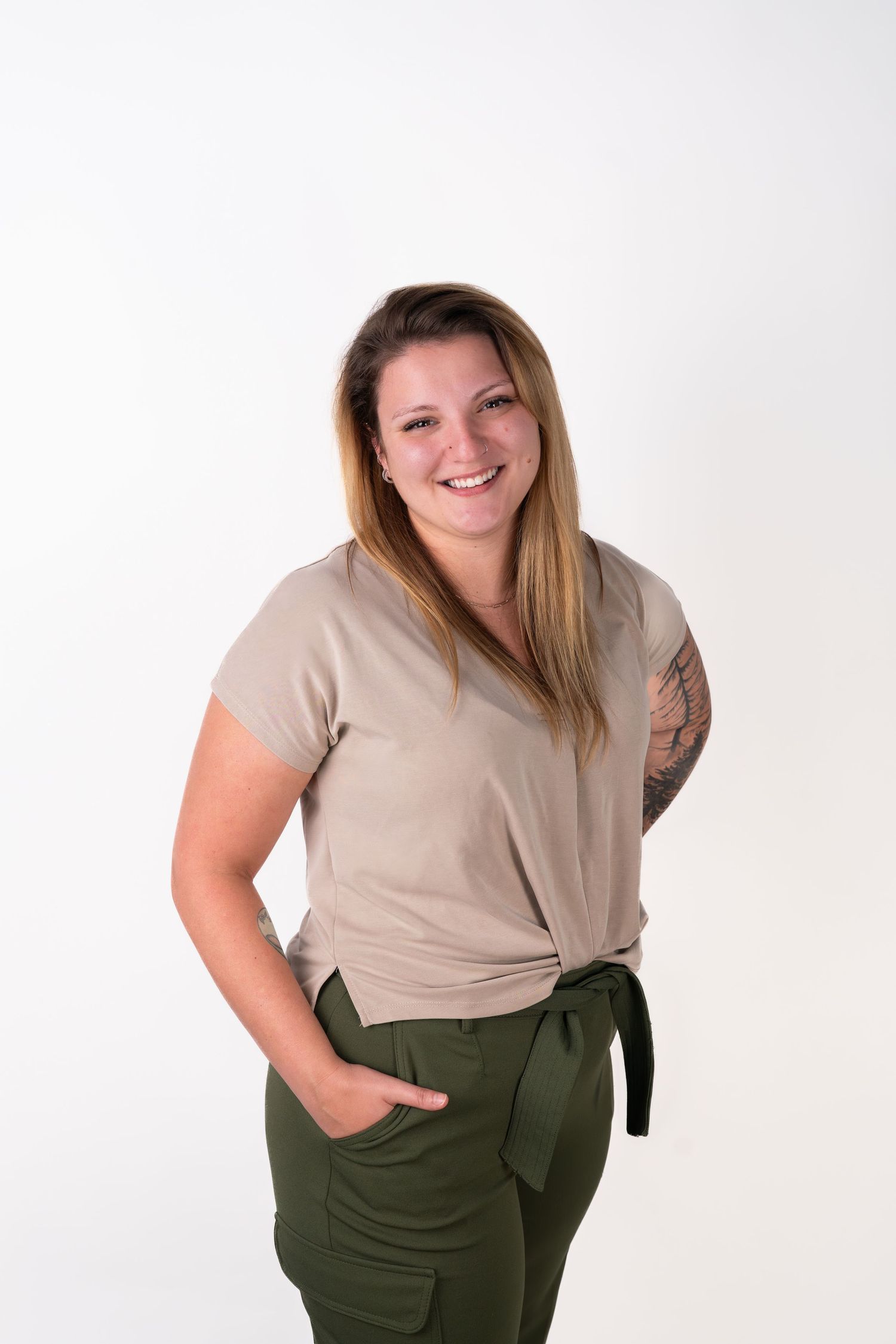 Person in beige top and olive pants poses casually against white studio background.