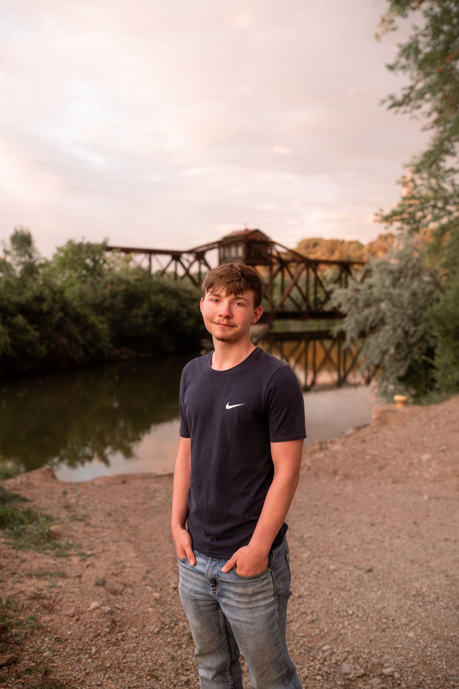 Person in Nike shirt stands near rustic bridge at sunset.