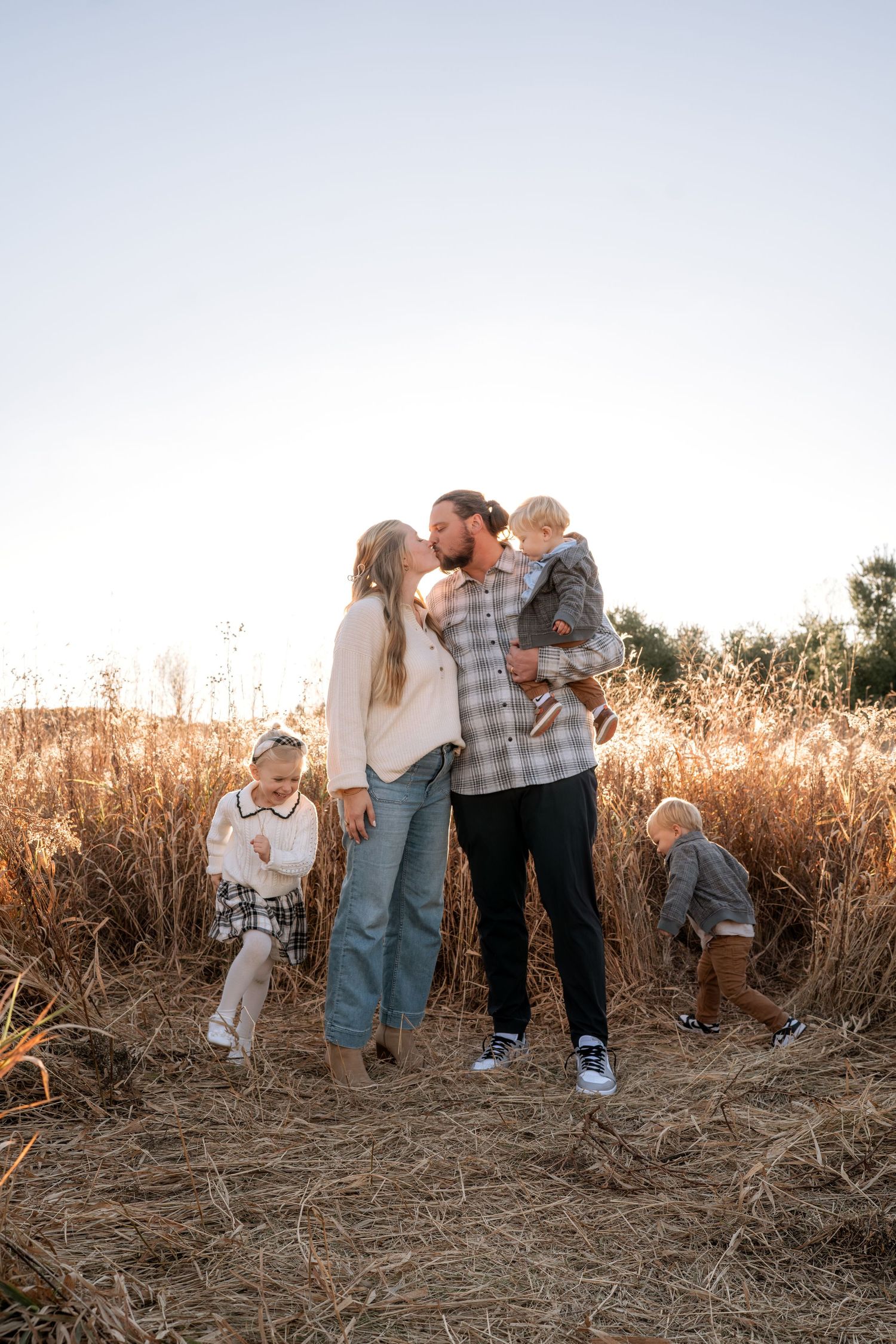 Family shares tender moments together in golden field at sunset.