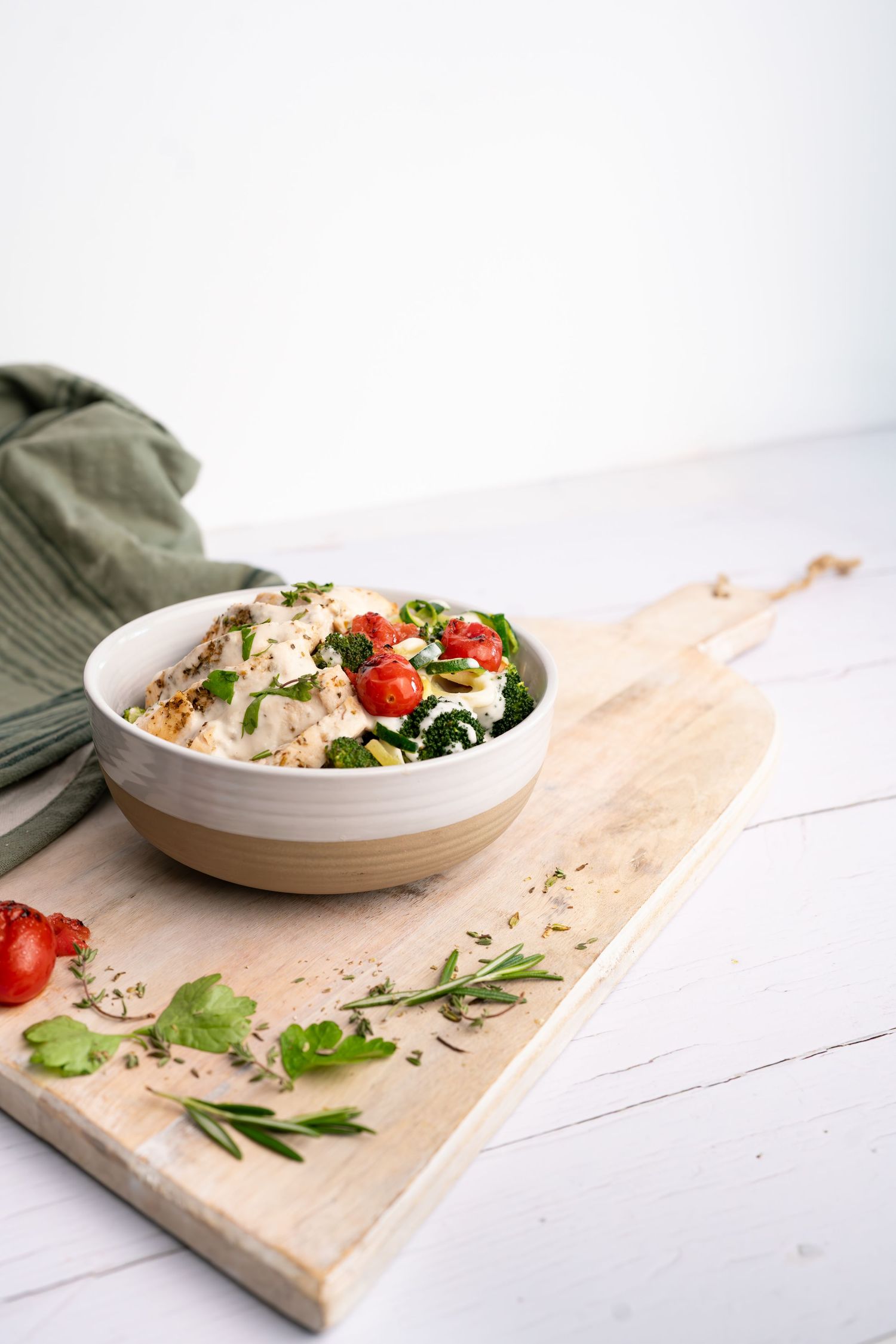 Healthy grain bowl with vegetables and protein served on a white wooden table with fresh herbs.