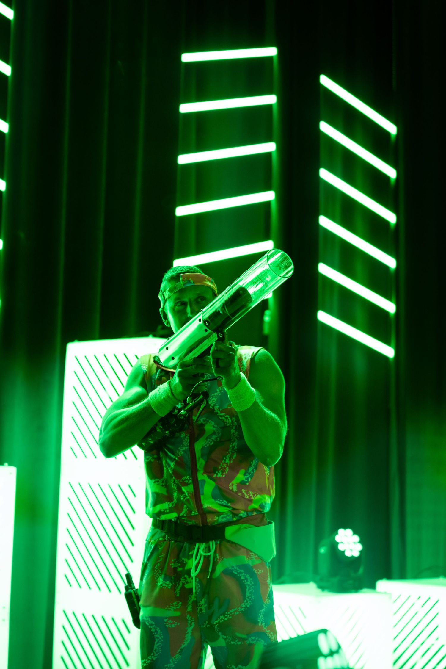 Concert performers silhouetted against dramatic green stage lighting and effects.