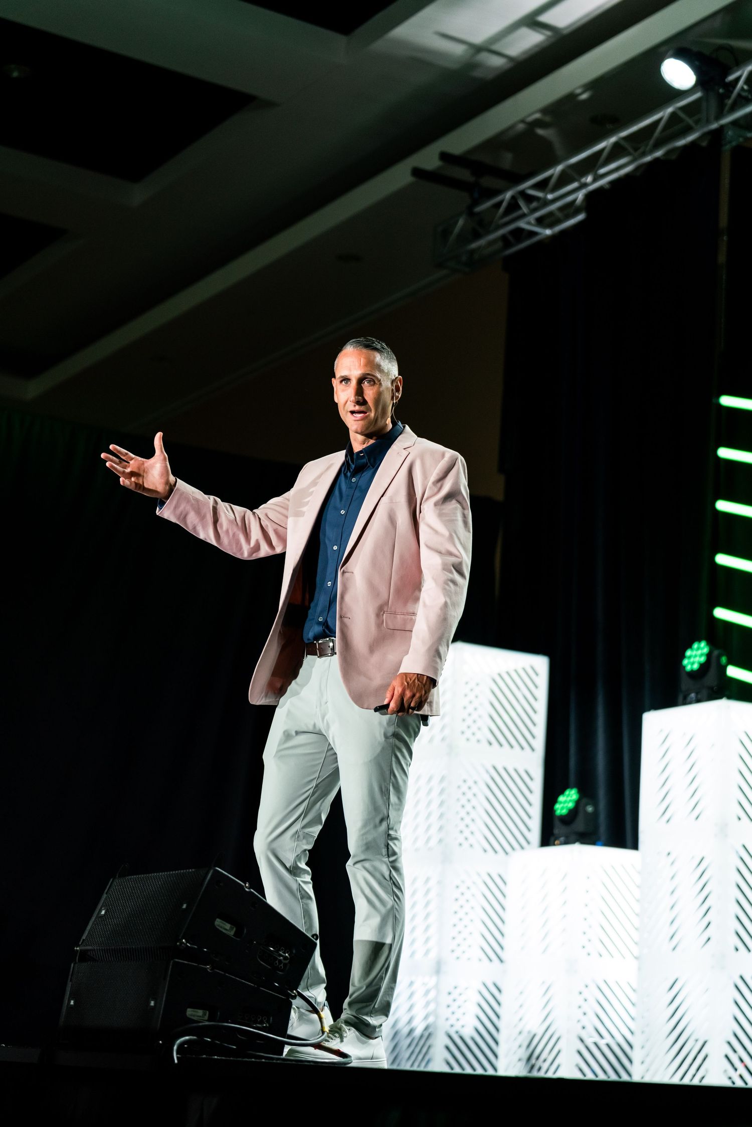 Professional speaker in light colored suit presenting on stage with dramatic lighting effects.
