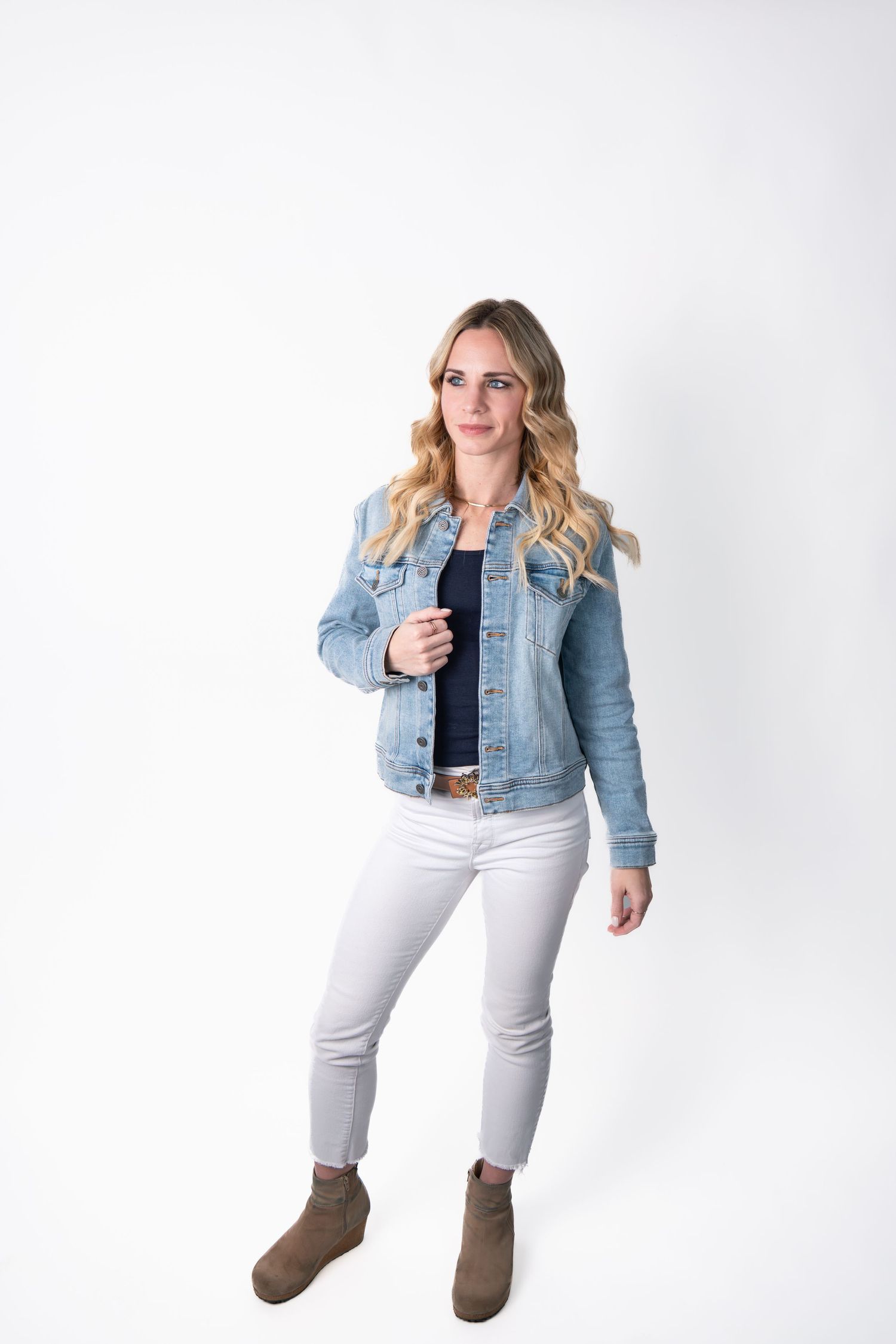 Woman in denim jacket and white pants strikes casual poses against white background.