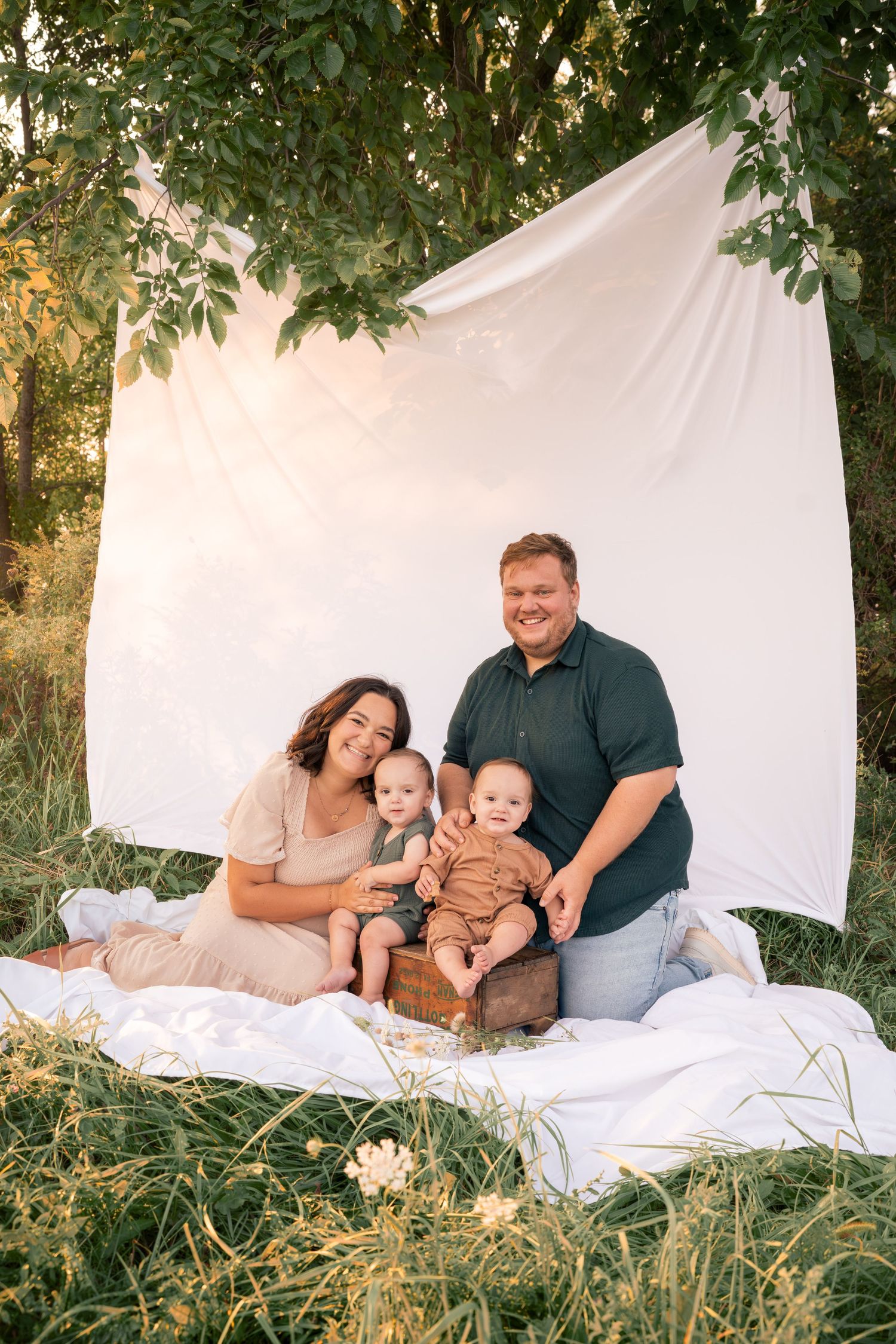Family portrait session on white blanket outdoors with small children and natural backdrop.