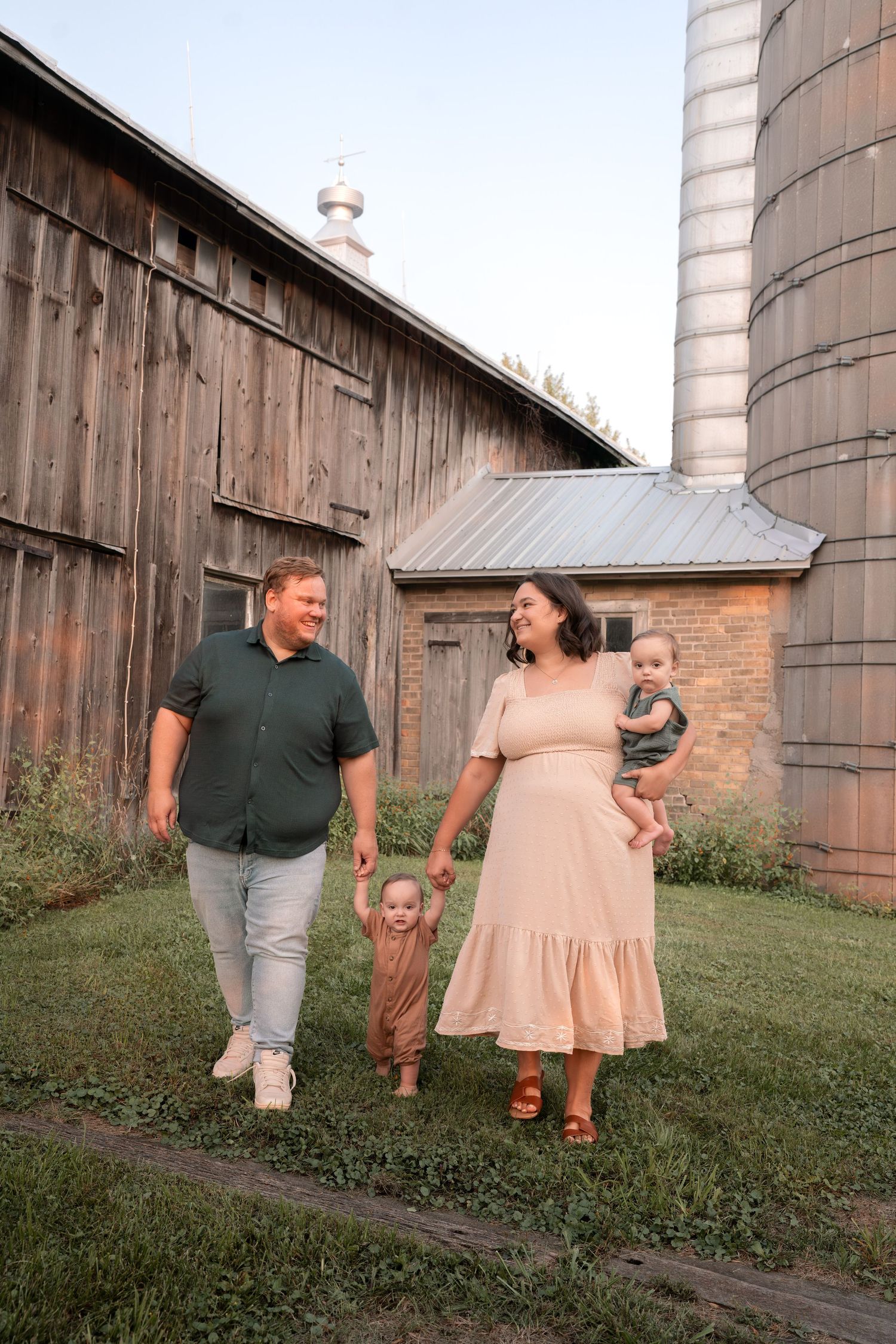 Family walking together near rustic wooden barns and silos at sunset.