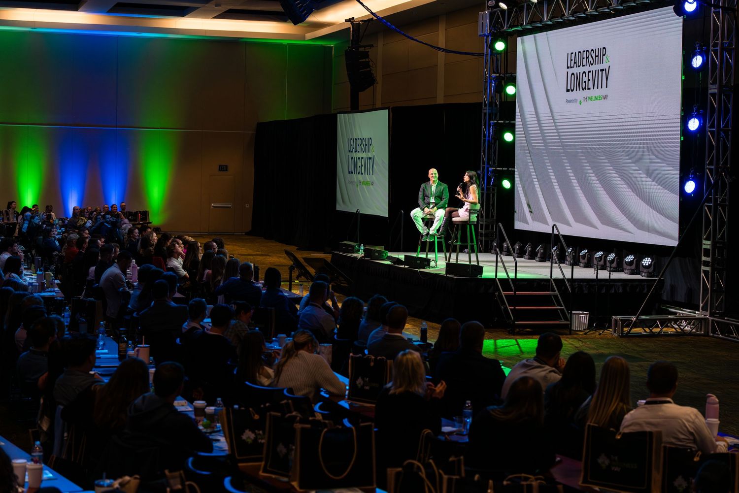 Conference hall with blue and green lighting setup showing presentation screen.