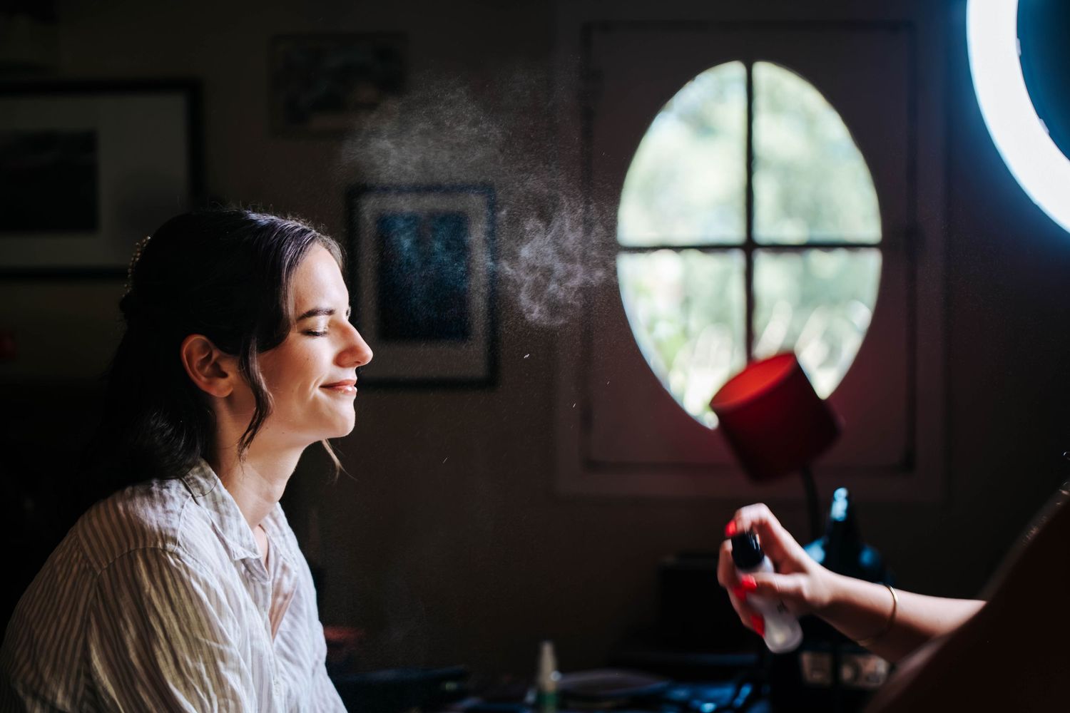 A bride getting her makeup set with a spray mist, illuminated by a ring light in a softly lit room.