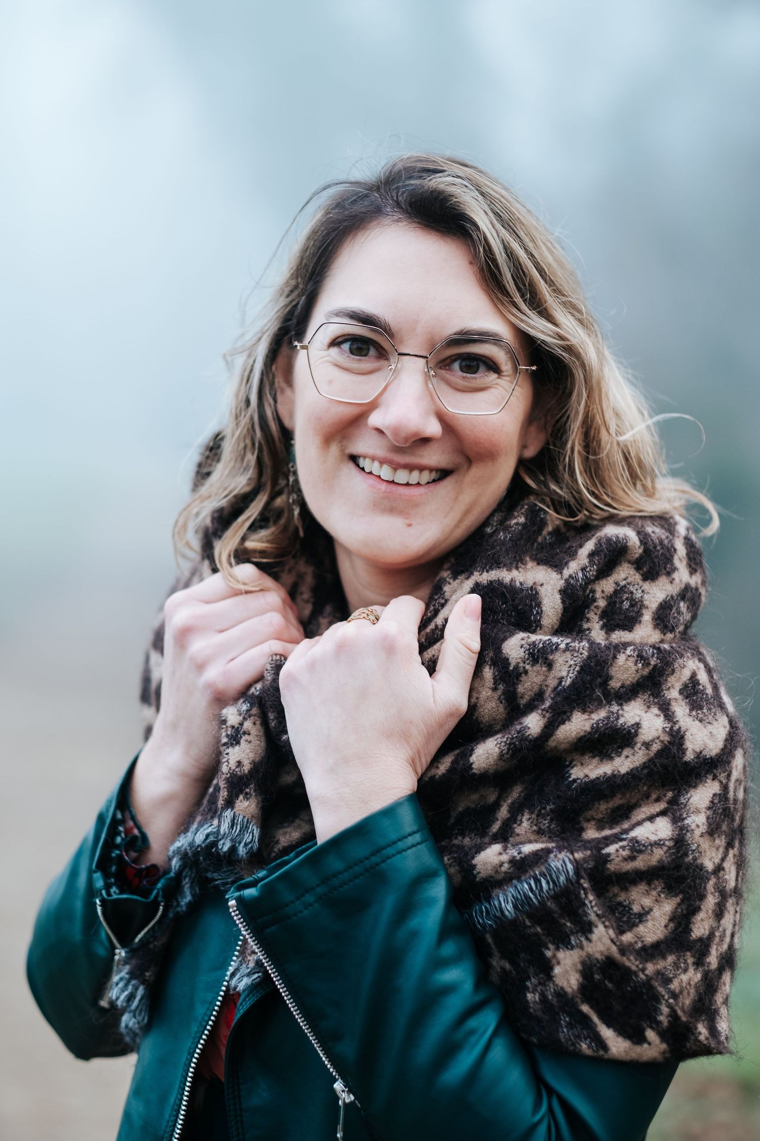 A person in a green jacket and animal print scarf poses playfully in a series of outdoor portrait shots.