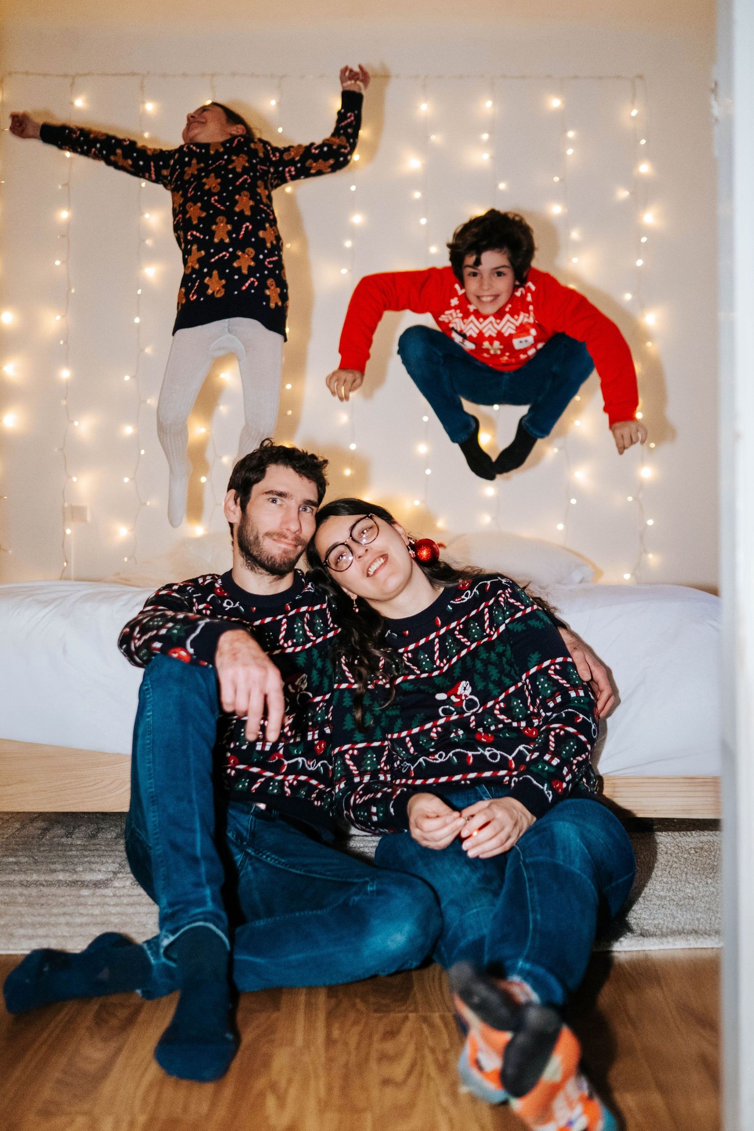A festive holiday photo with people wearing matching Christmas sweaters posing against a backdrop of twinkling lights.
