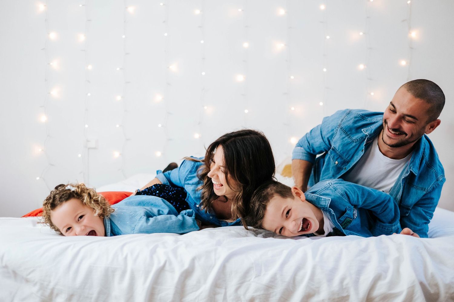 Family members in matching blue denim outfits laying on white sheets while playing and laughing together.