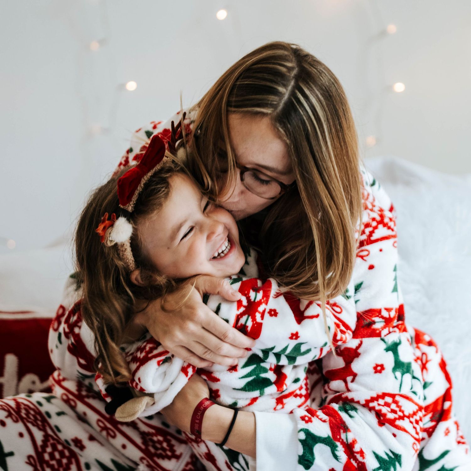 Person wearing festive holiday sweater laughs joyfully while lying on white backdrop with Christmas decorations.