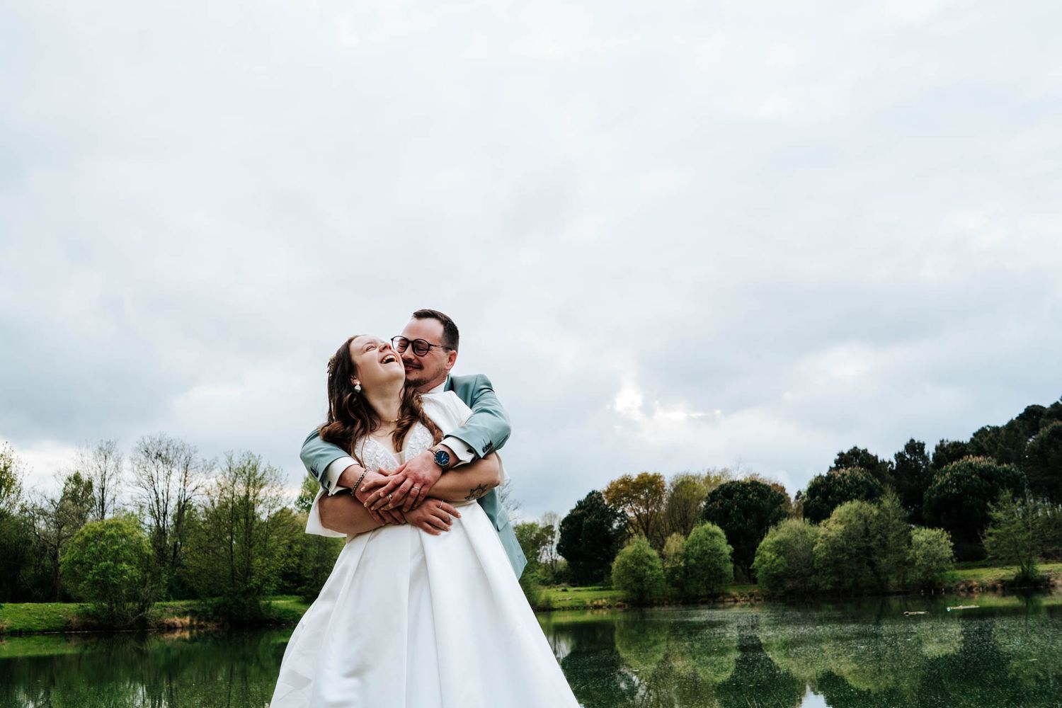 Romantic couple embracing in a serene countryside setting with lush green trees.