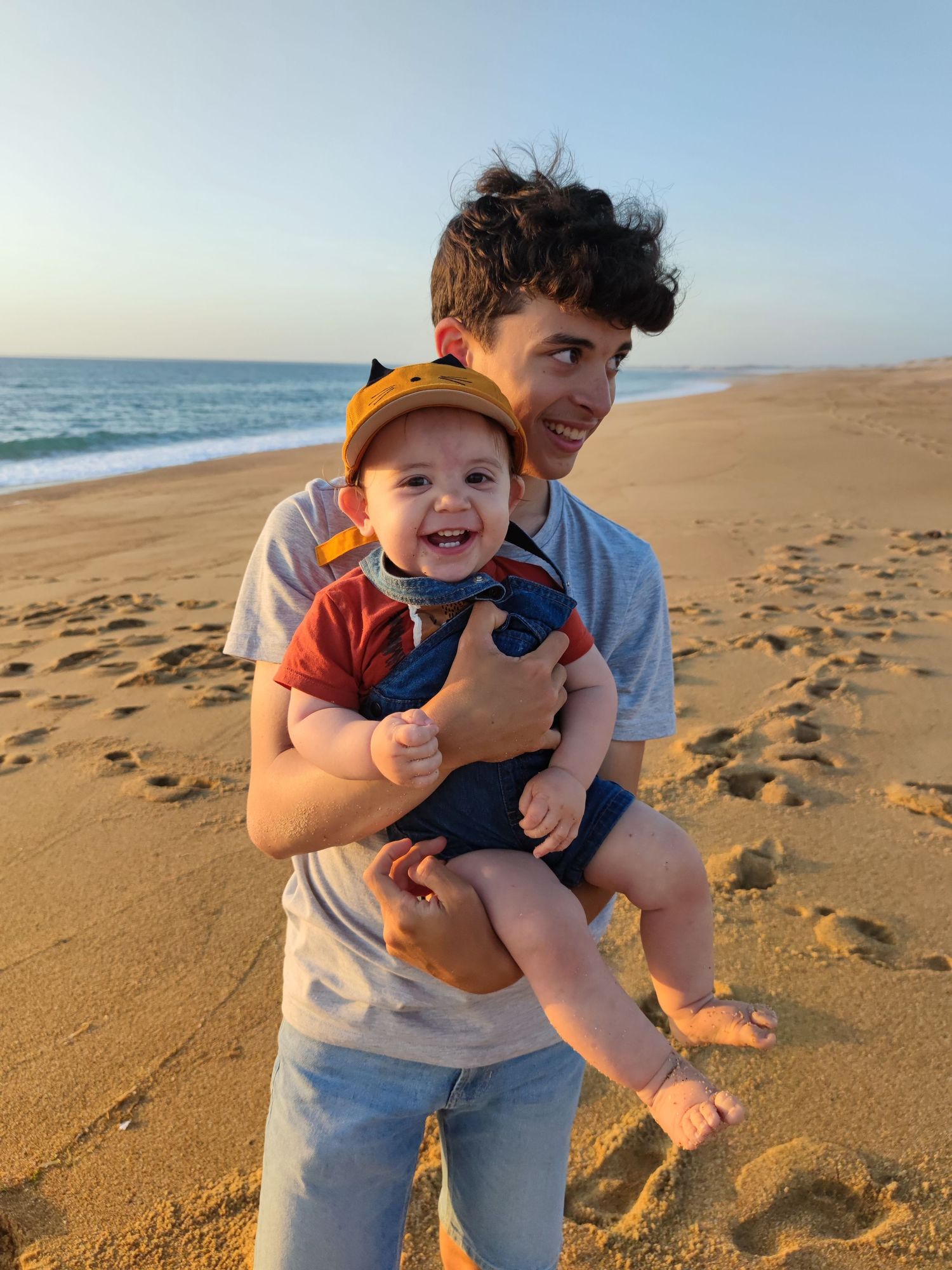 Parent and child enjoy a sunny afternoon walking along a sandy beach with footprints visible in golden sand.