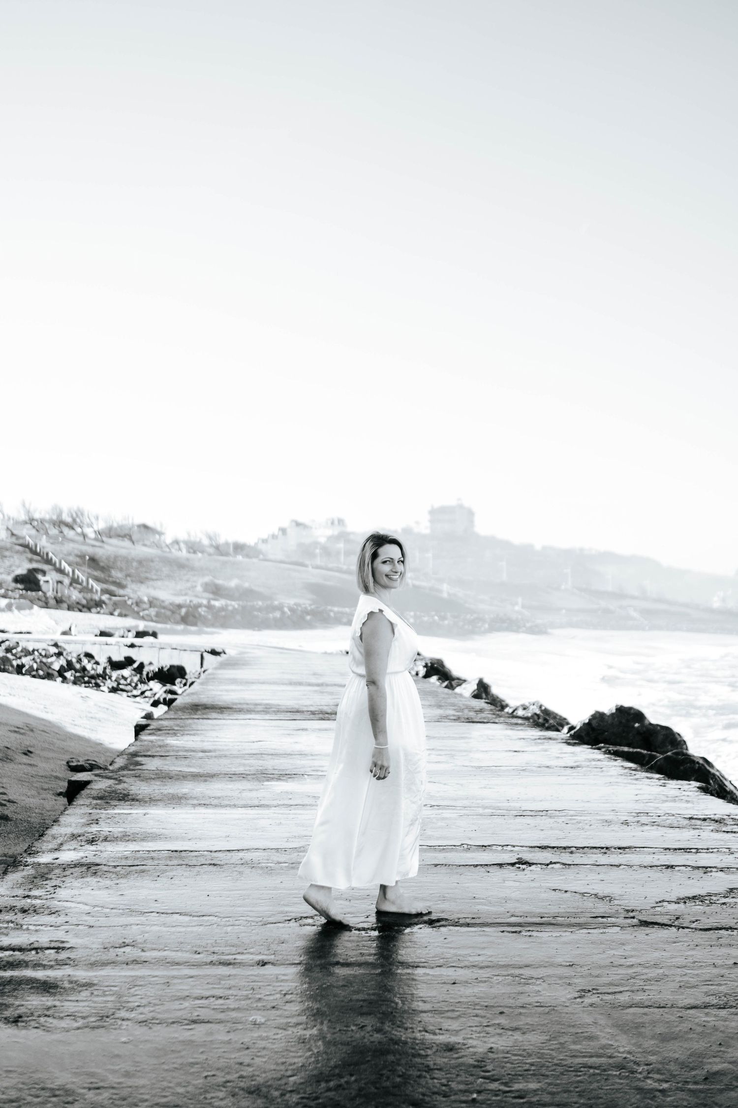 A series of black and white beach photos showing a figure in white walking through shallow ocean waves.