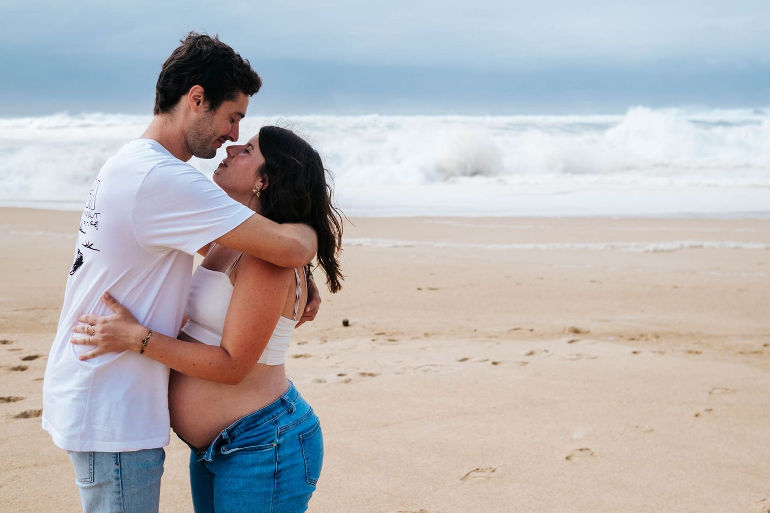 A couple shares romantic moments on a sandy beach with ocean waves in the background.