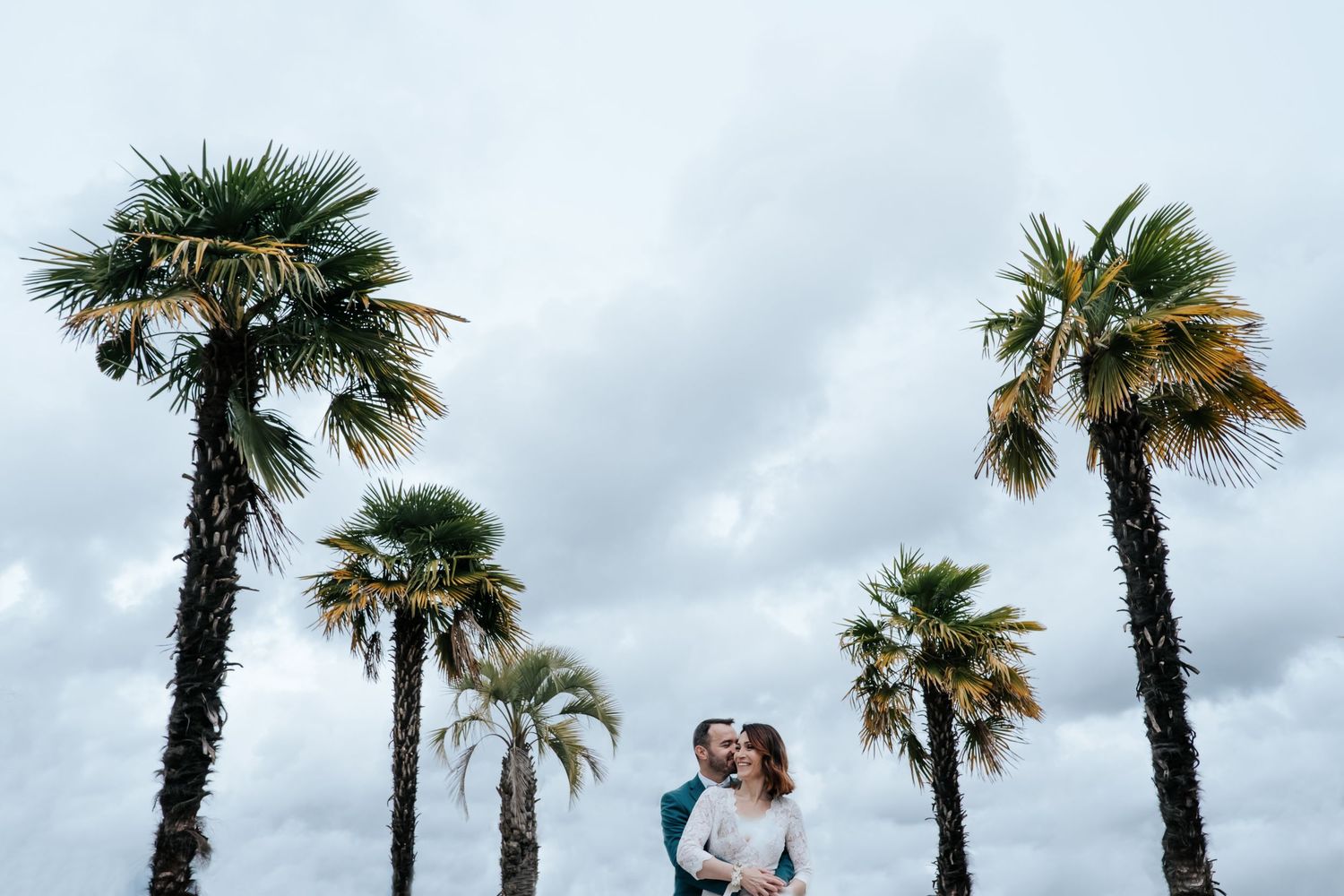 Palm trees line a cloudy beach setting during a romantic moment.